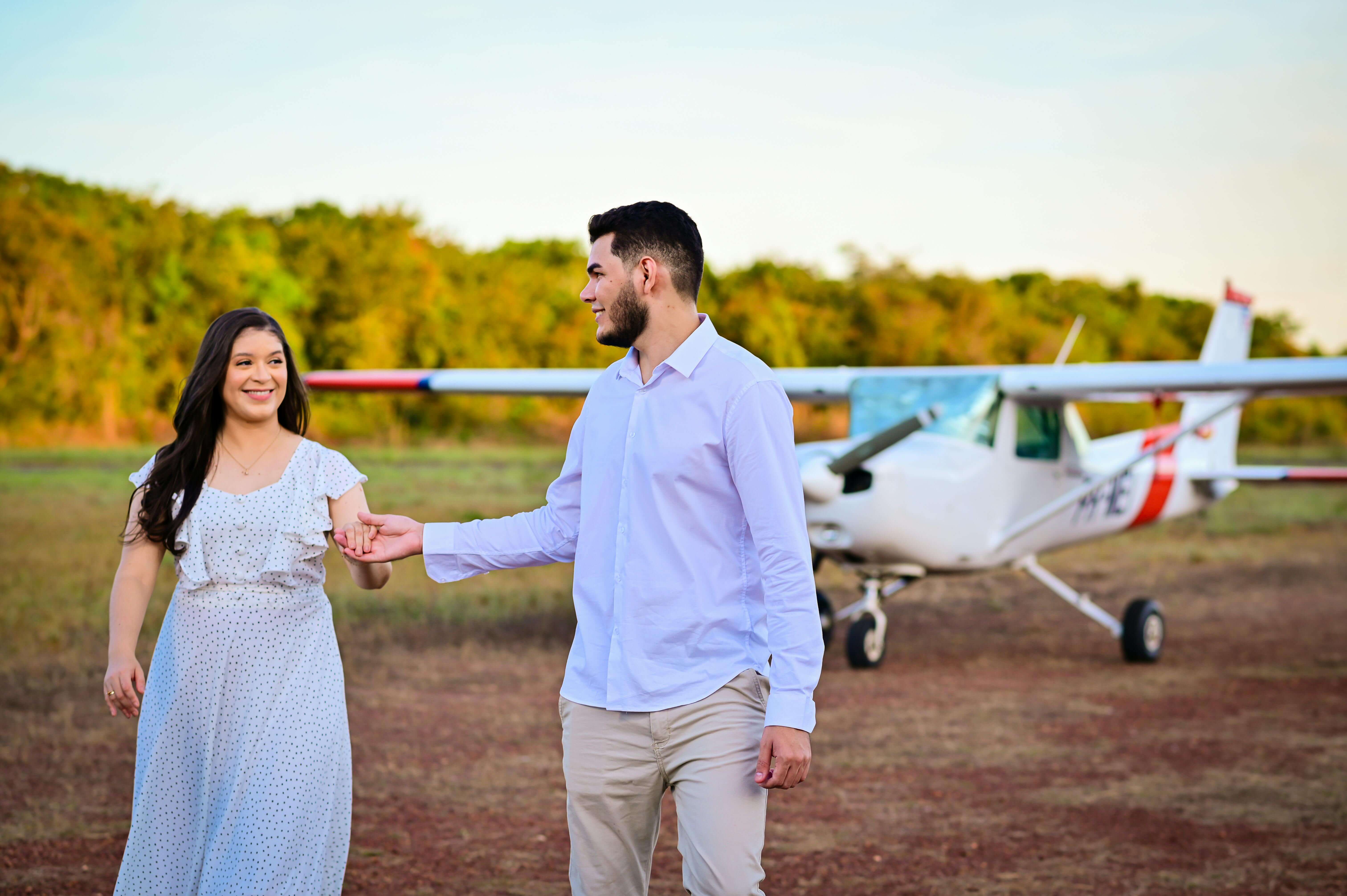 Smiling couple walking together holding hands near a private airplane outdoors.