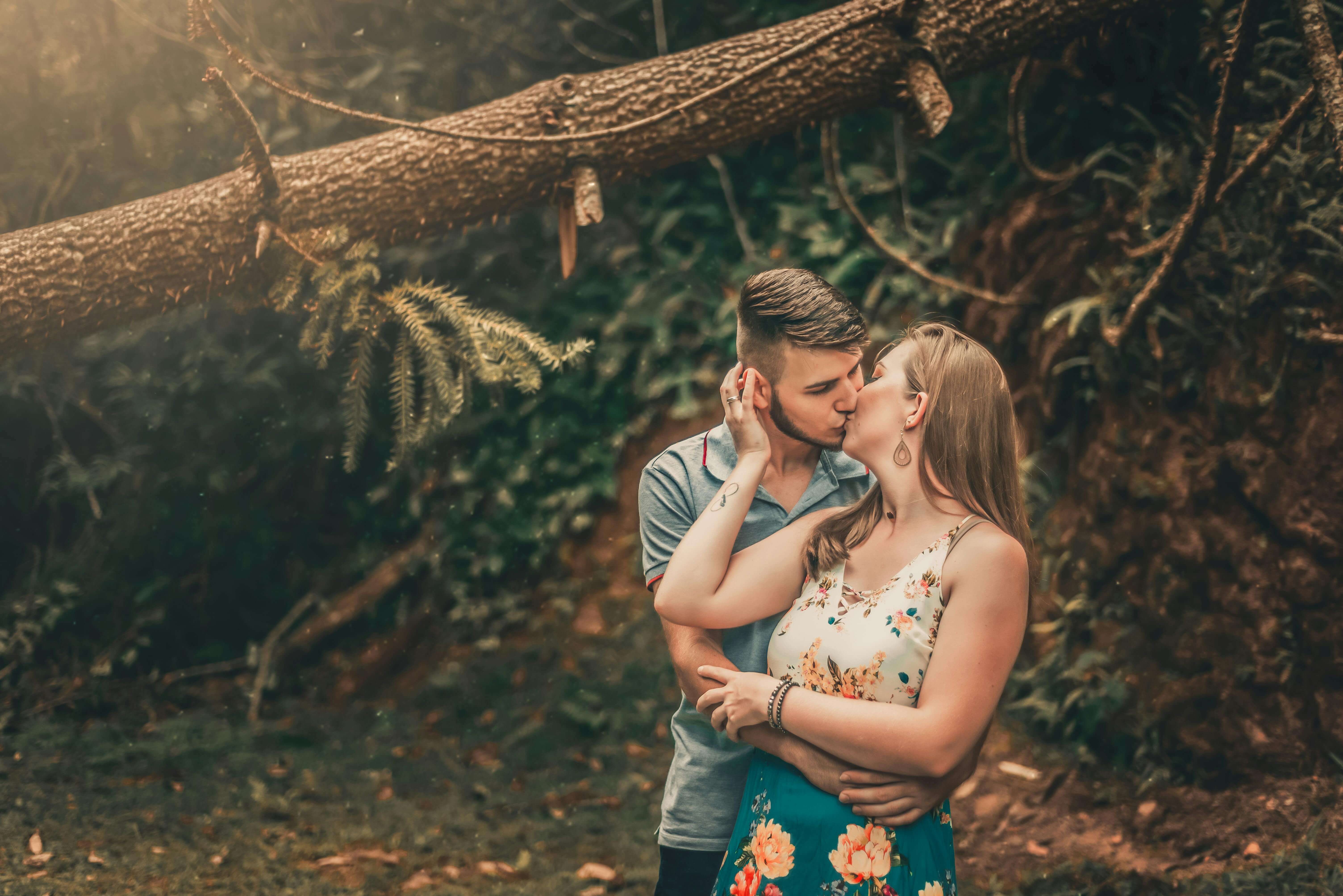 A couple shares a romantic kiss surrounded by lush forest scenery, adding a touch of nature and intimacy.