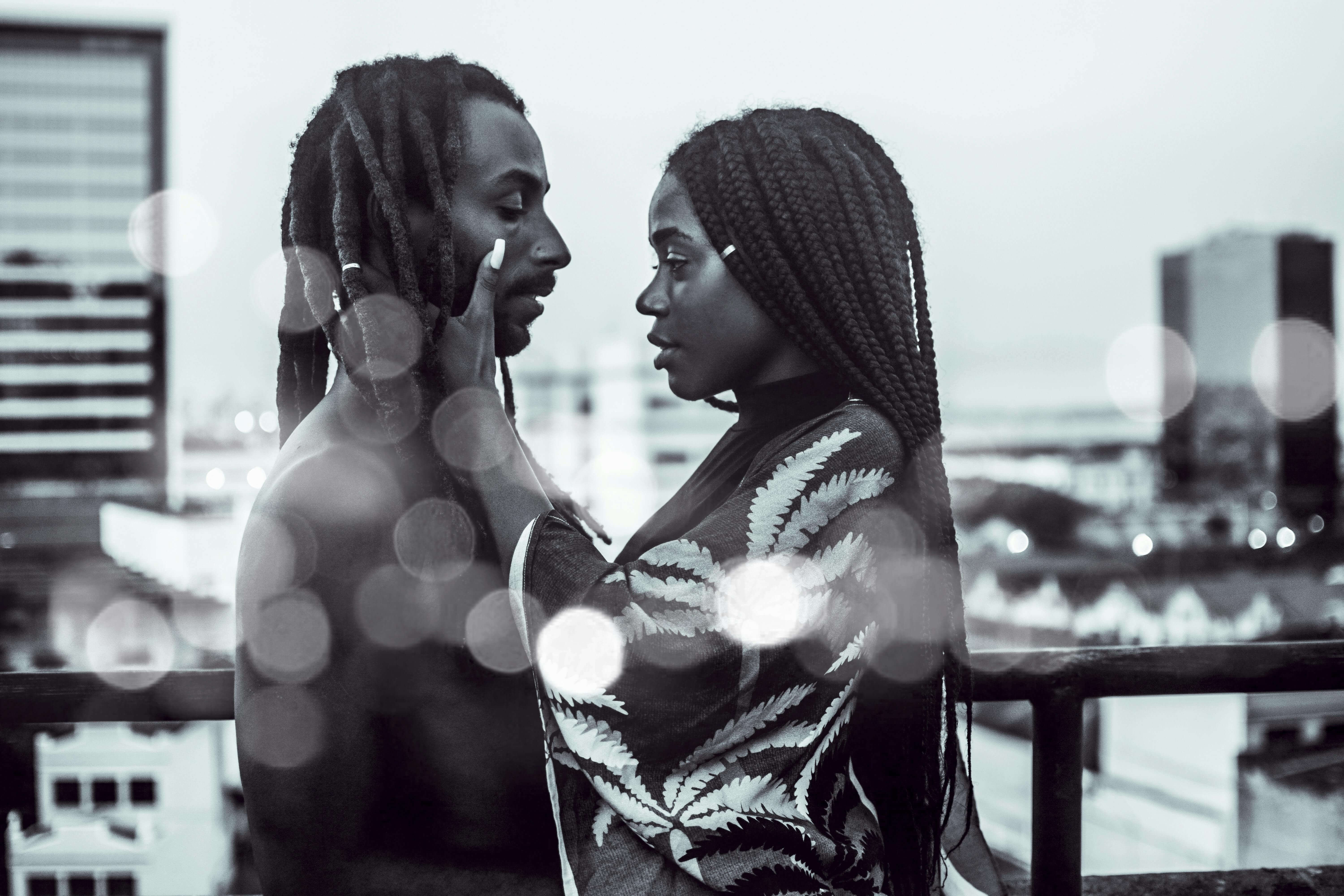 A romantic black and white photo of a couple embracing on a city rooftop with bokeh effect.