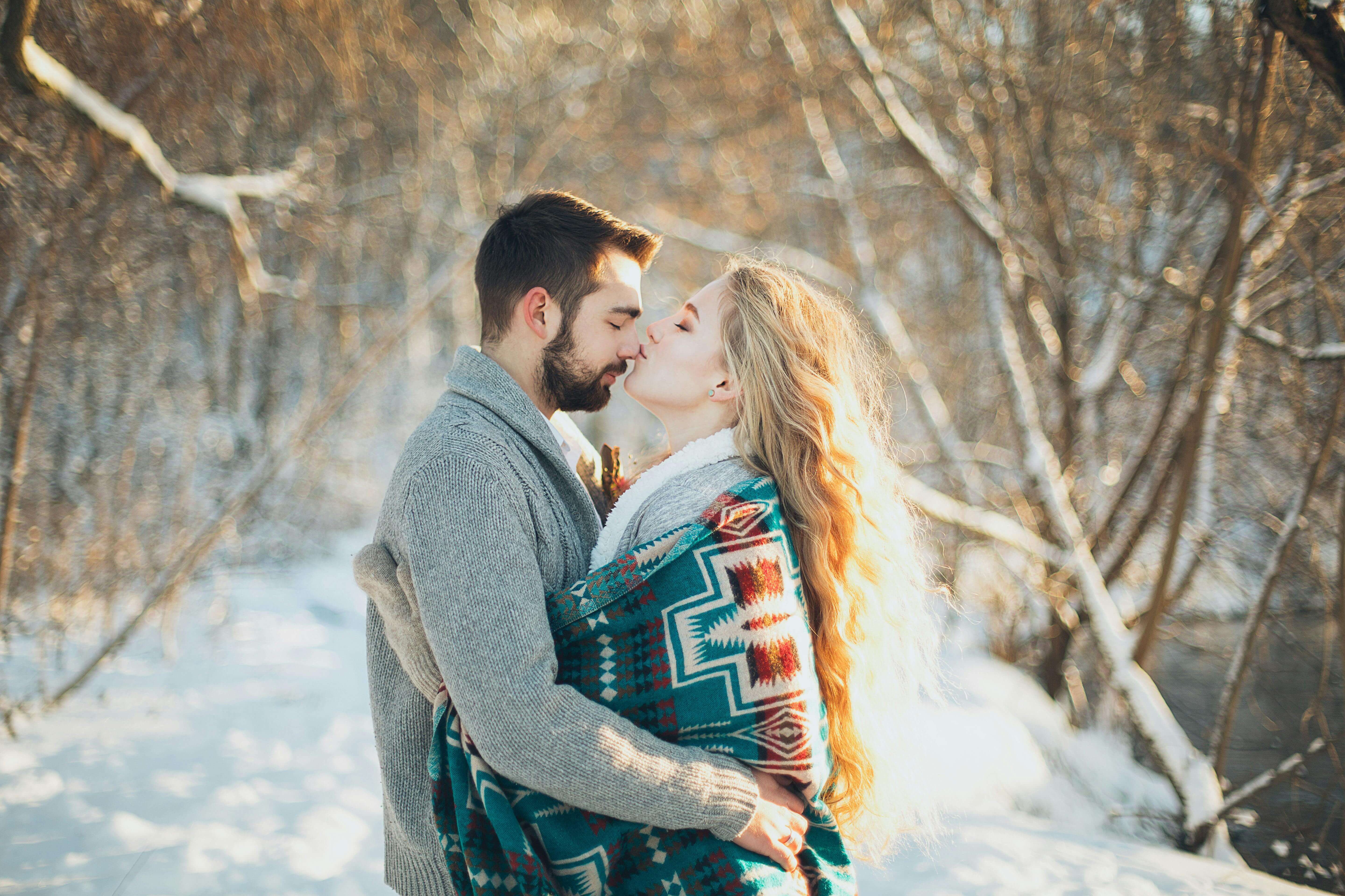 A couple shares a warm embrace in a snowy park setting, showing affection and togetherness.