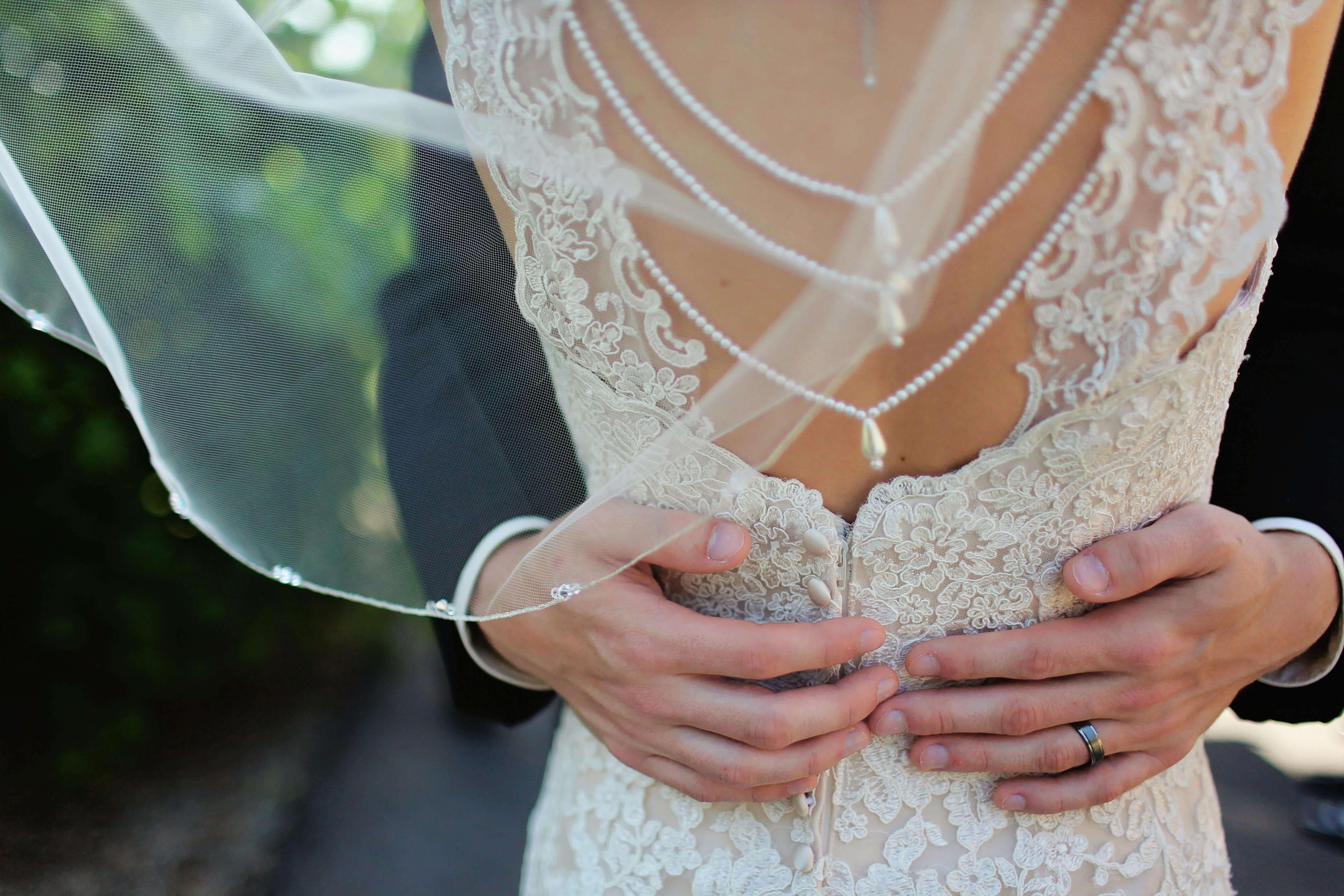 Close-up of bride and groom's embrace highlighting elegant lace bridal gown and pearl jewelry.