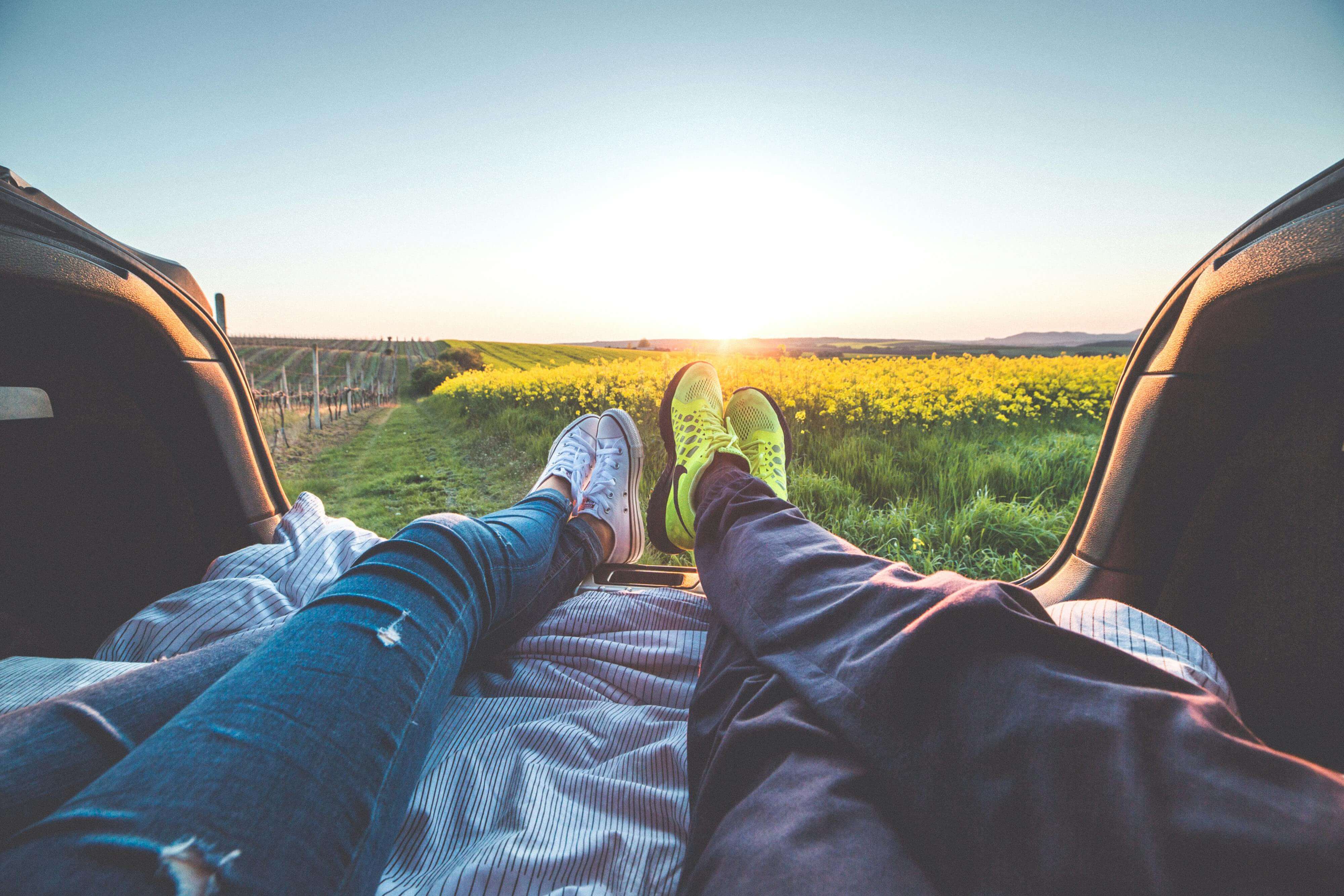 A couple relaxing in a car trunk enjoying a romantic sunset over fields.
