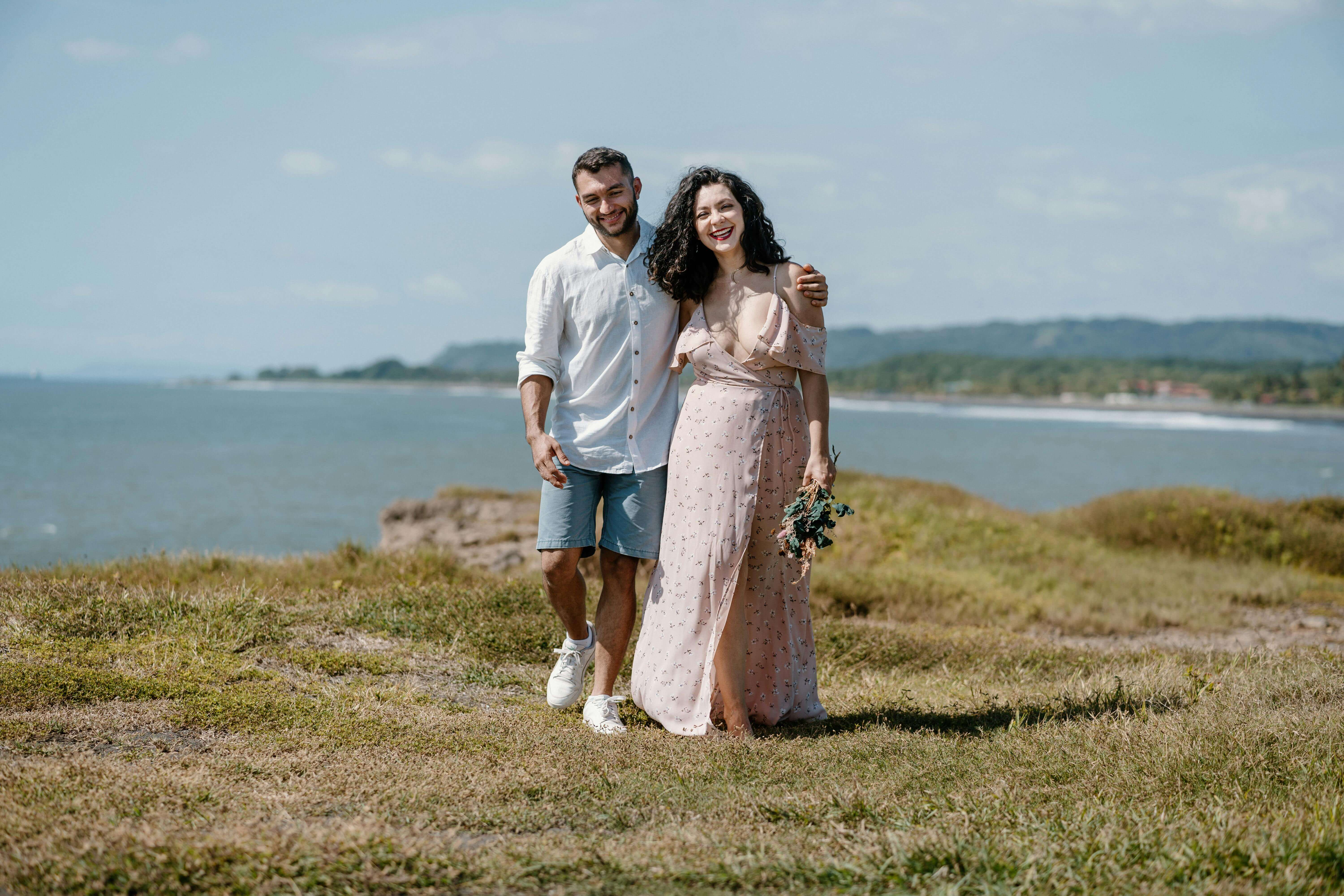Happy couple walking hand in hand on a coastal meadow with ocean in background.