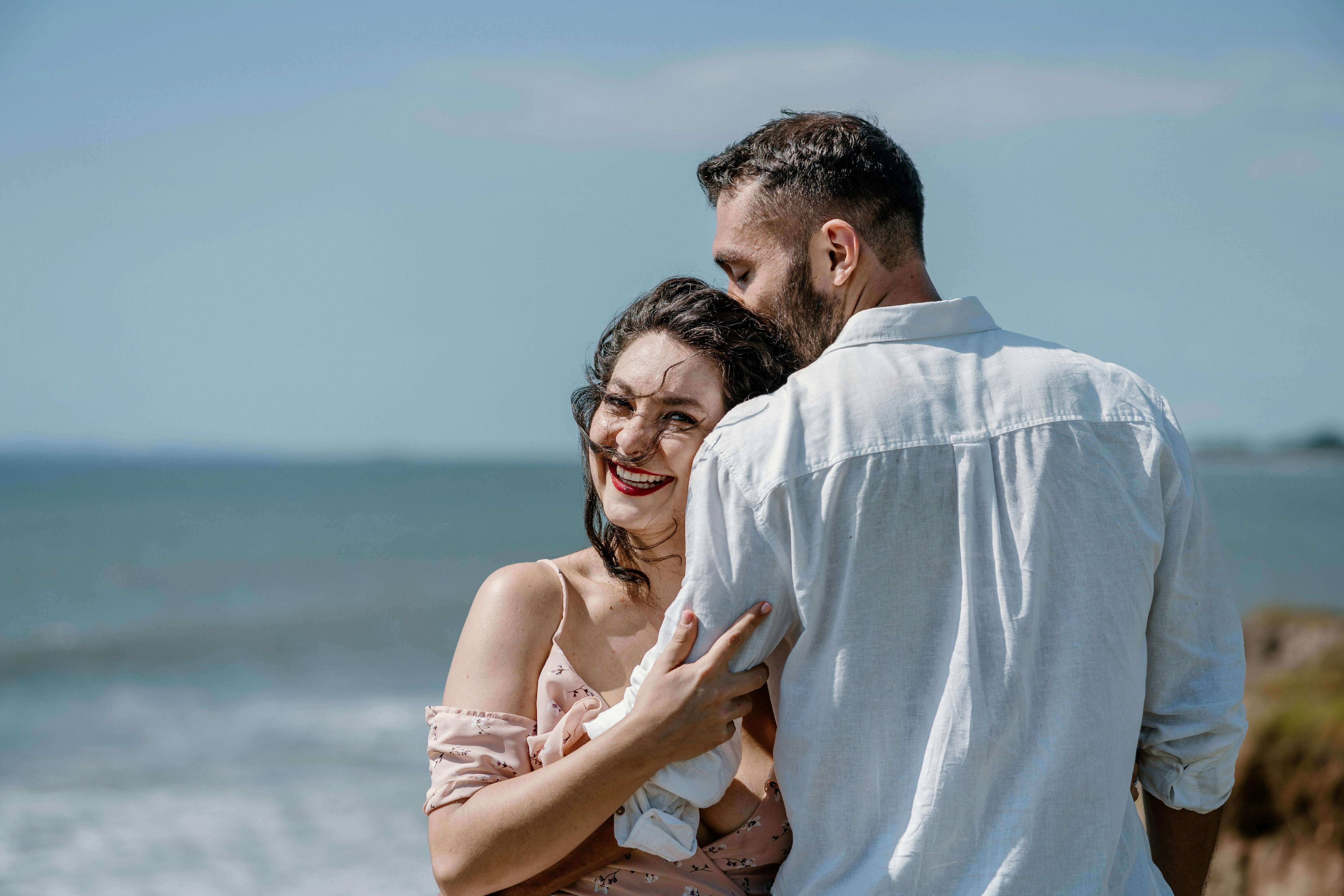 Joyful couple embracing by the sea on a sunny day, expressing love and happiness.