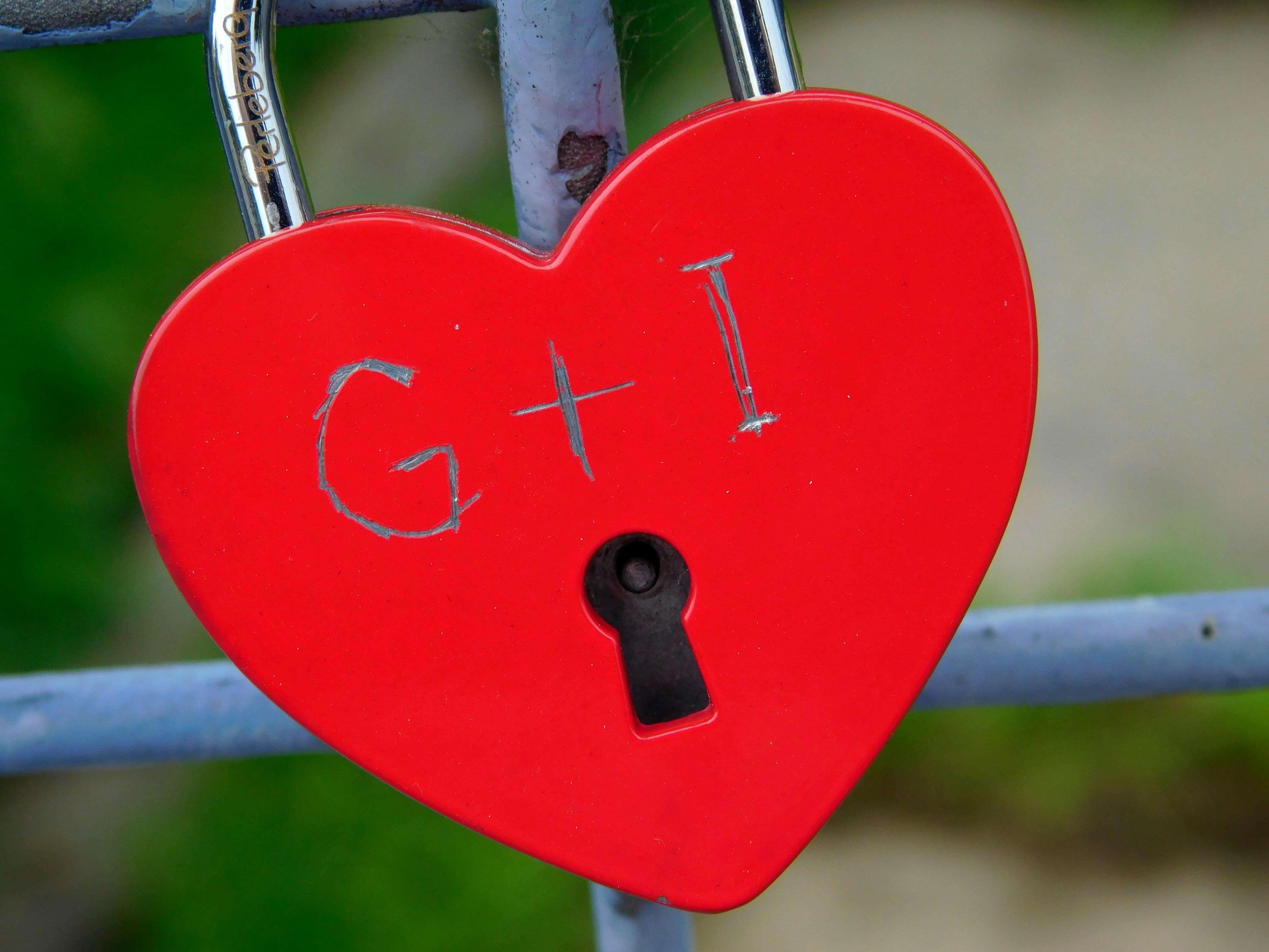 A red heart-shaped padlock symbolizes love and commitment, attached to a metal fence outdoors.