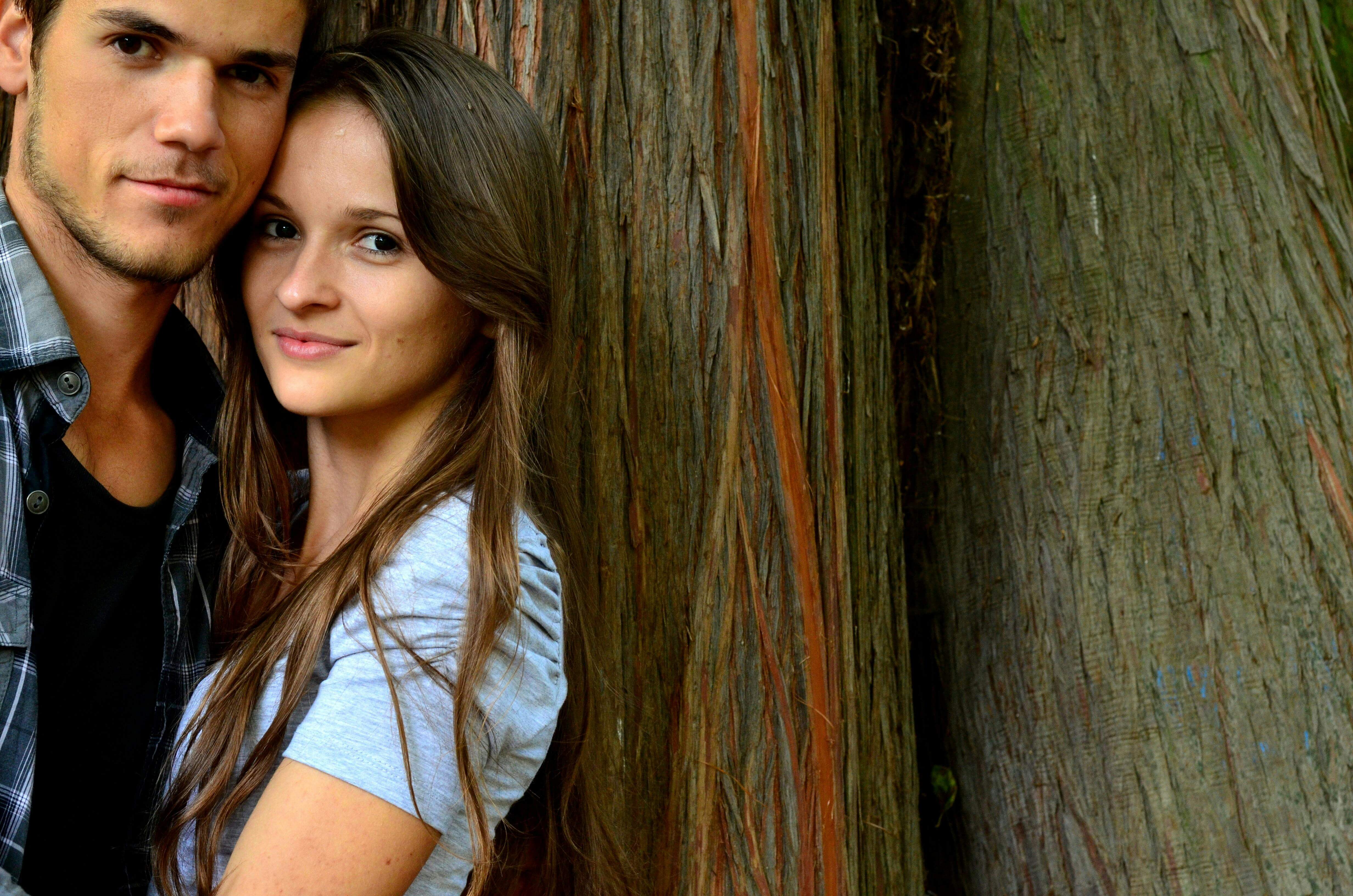 Young couple embracing outdoors against a rustic wooden background, conveying love and connection.