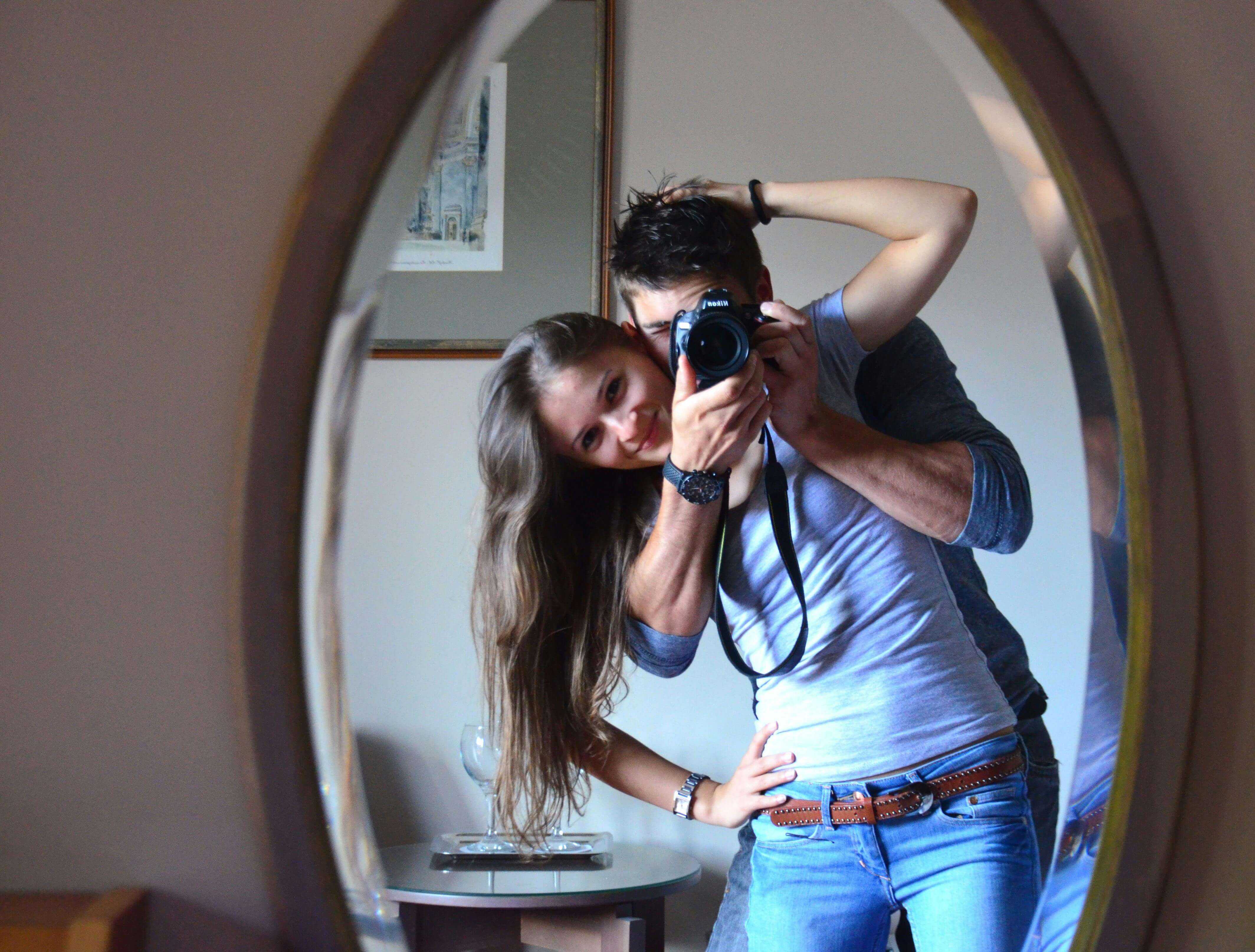 Smiling couple capturing a joyful moment with a mirror selfie indoors.