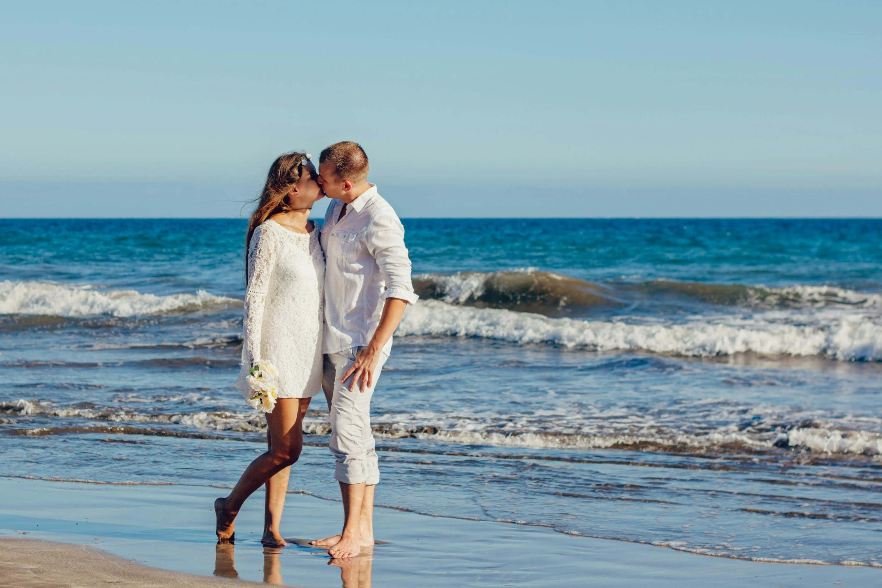 A couple enjoys a romantic kiss on a sunny beach, embracing love by the sea.