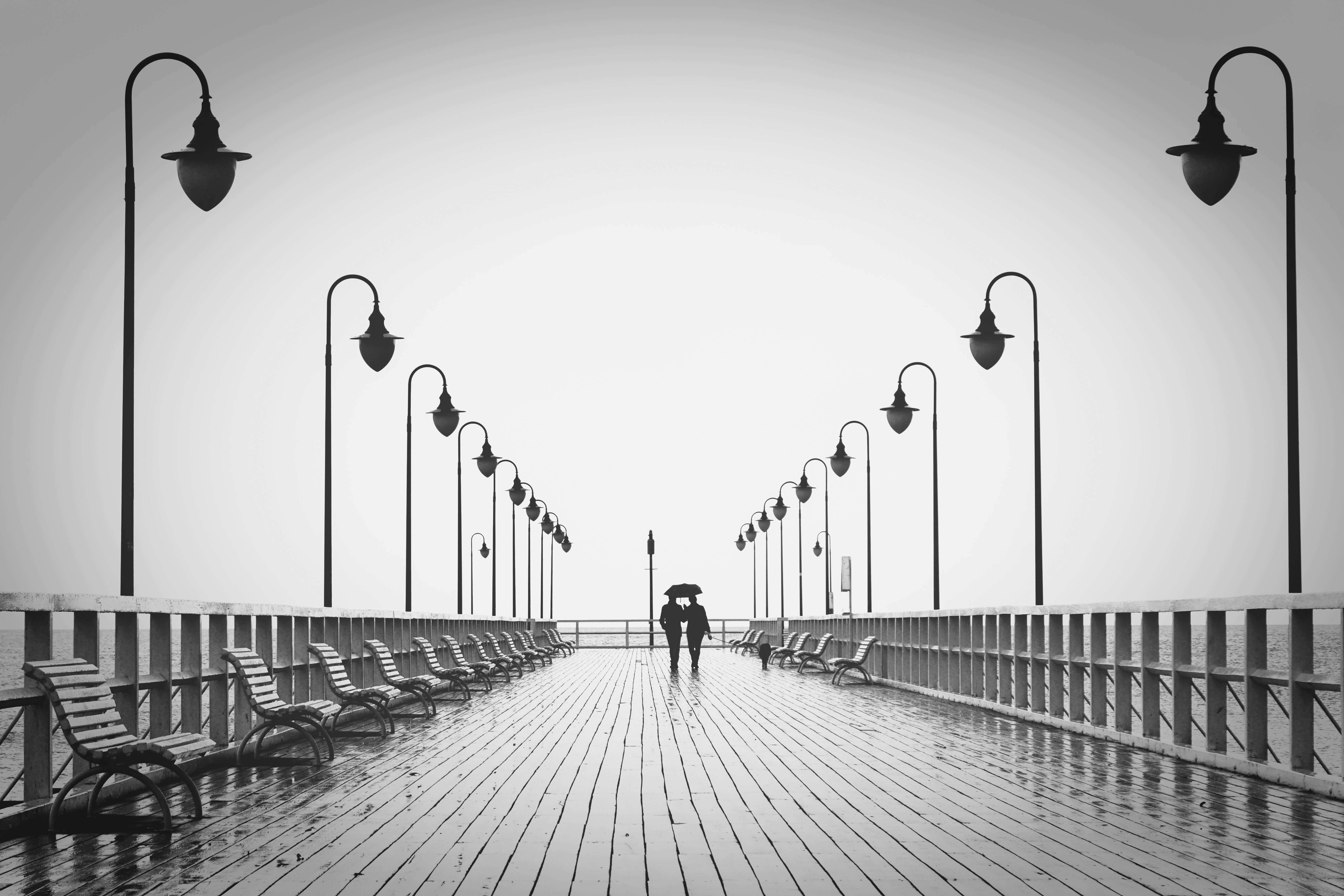 A couple holding umbrellas walks on a rainy boardwalk, embodying romance and tranquility.