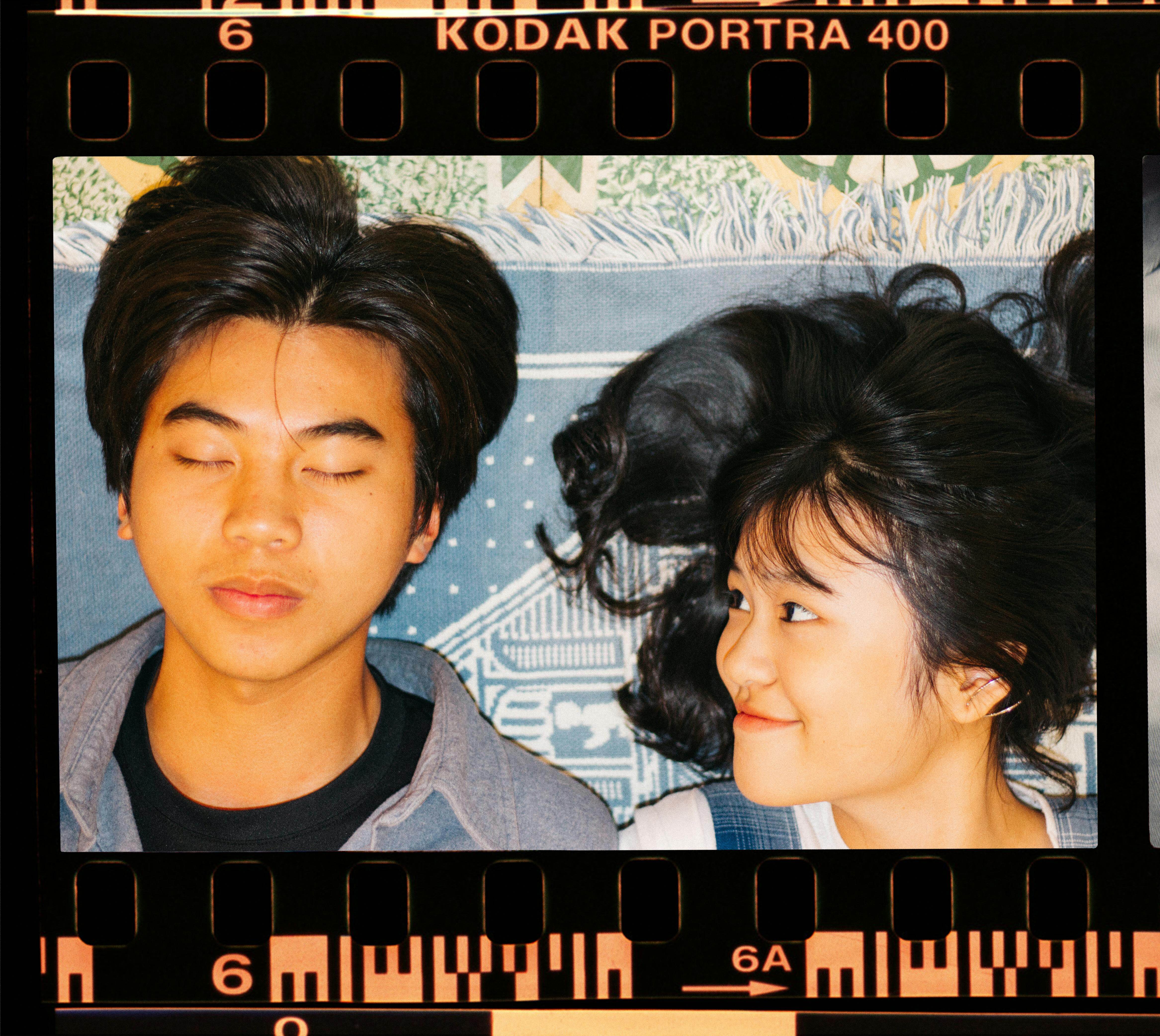 Young couple with playful expressions lies down against a creative backdrop on film frame.