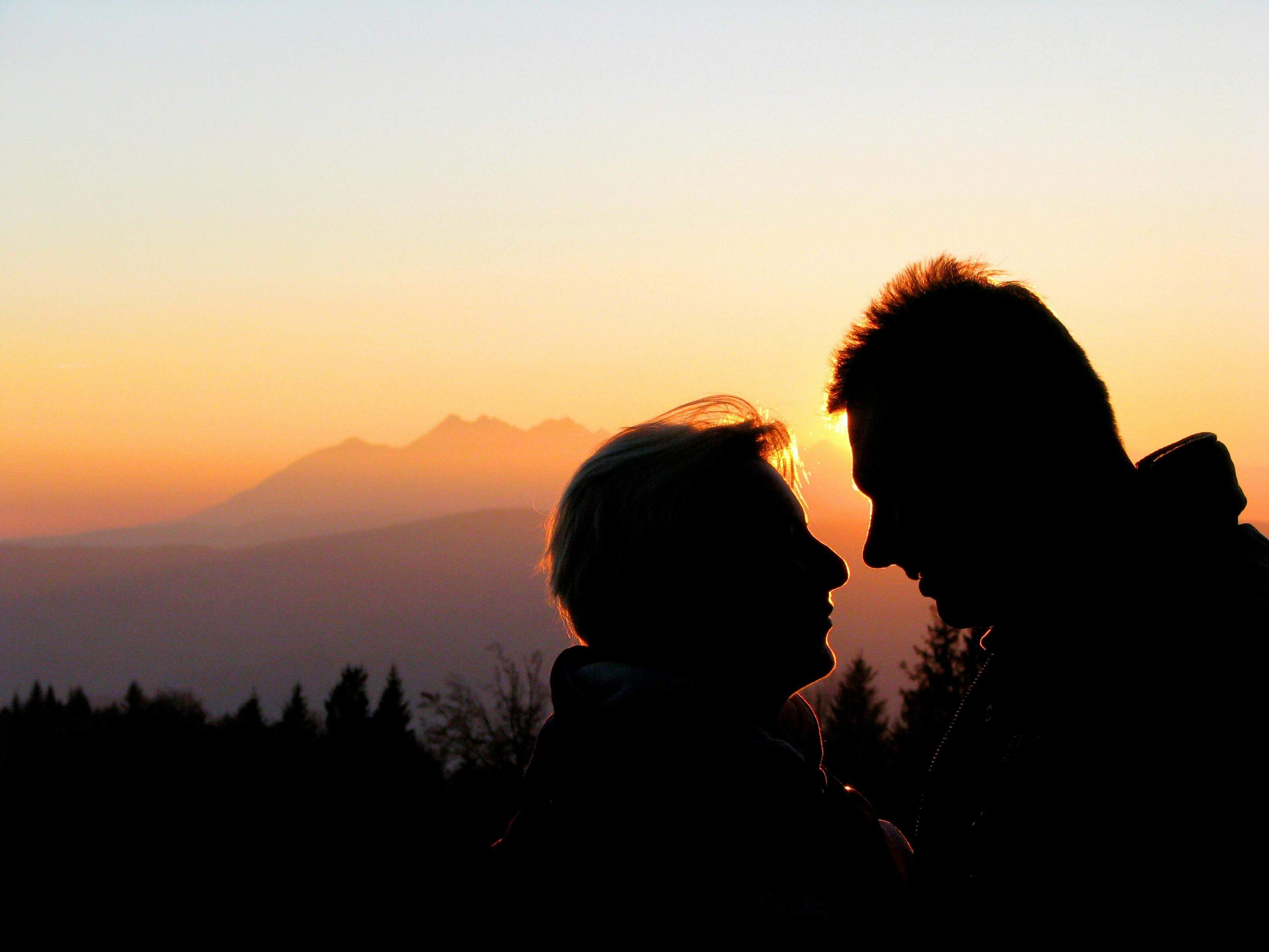 Silhouette of a couple sharing a tender moment against a mountain sunset.