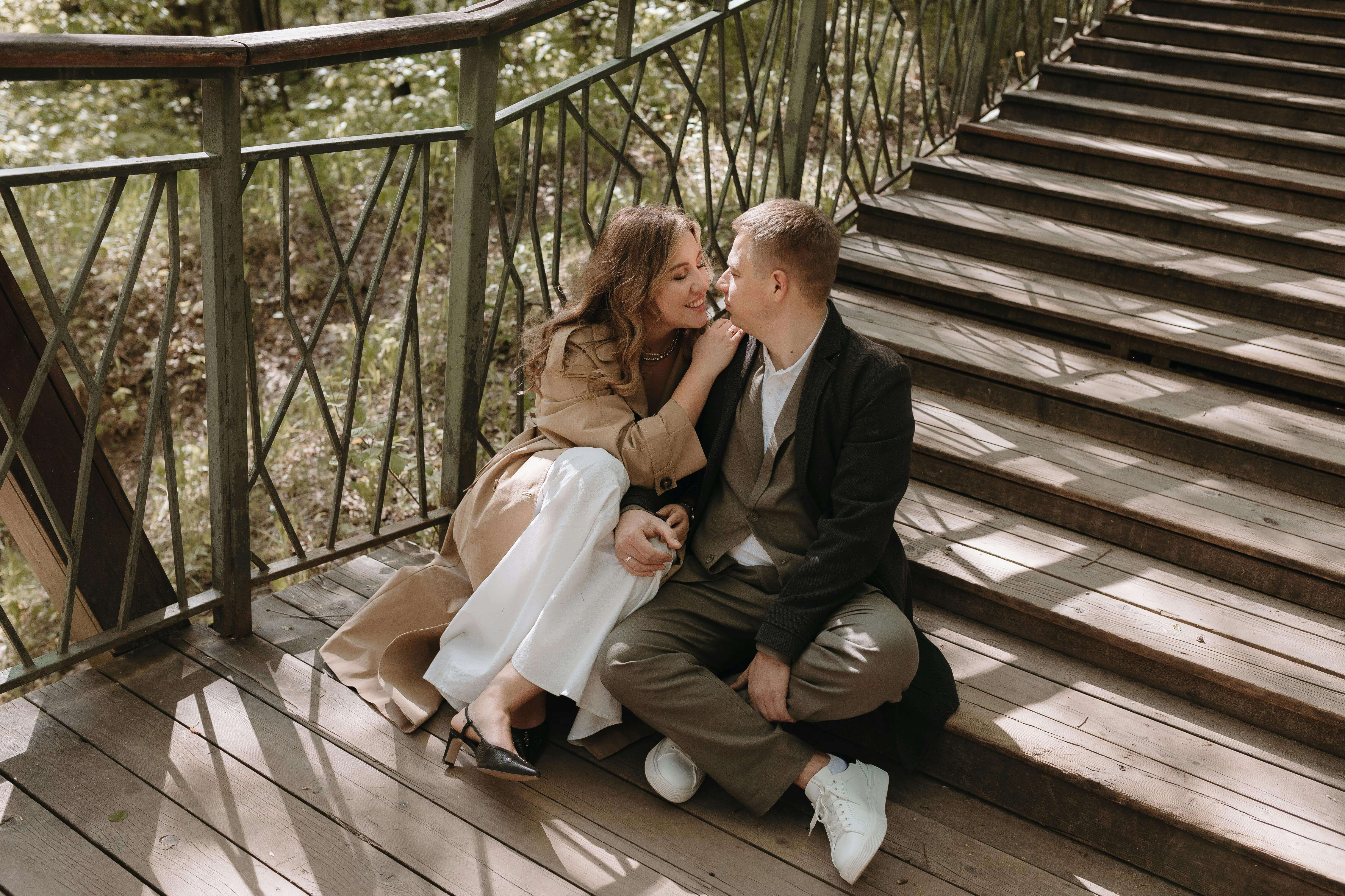 A couple enjoying a tender moment on a wooden bridge in a sunny park setting.