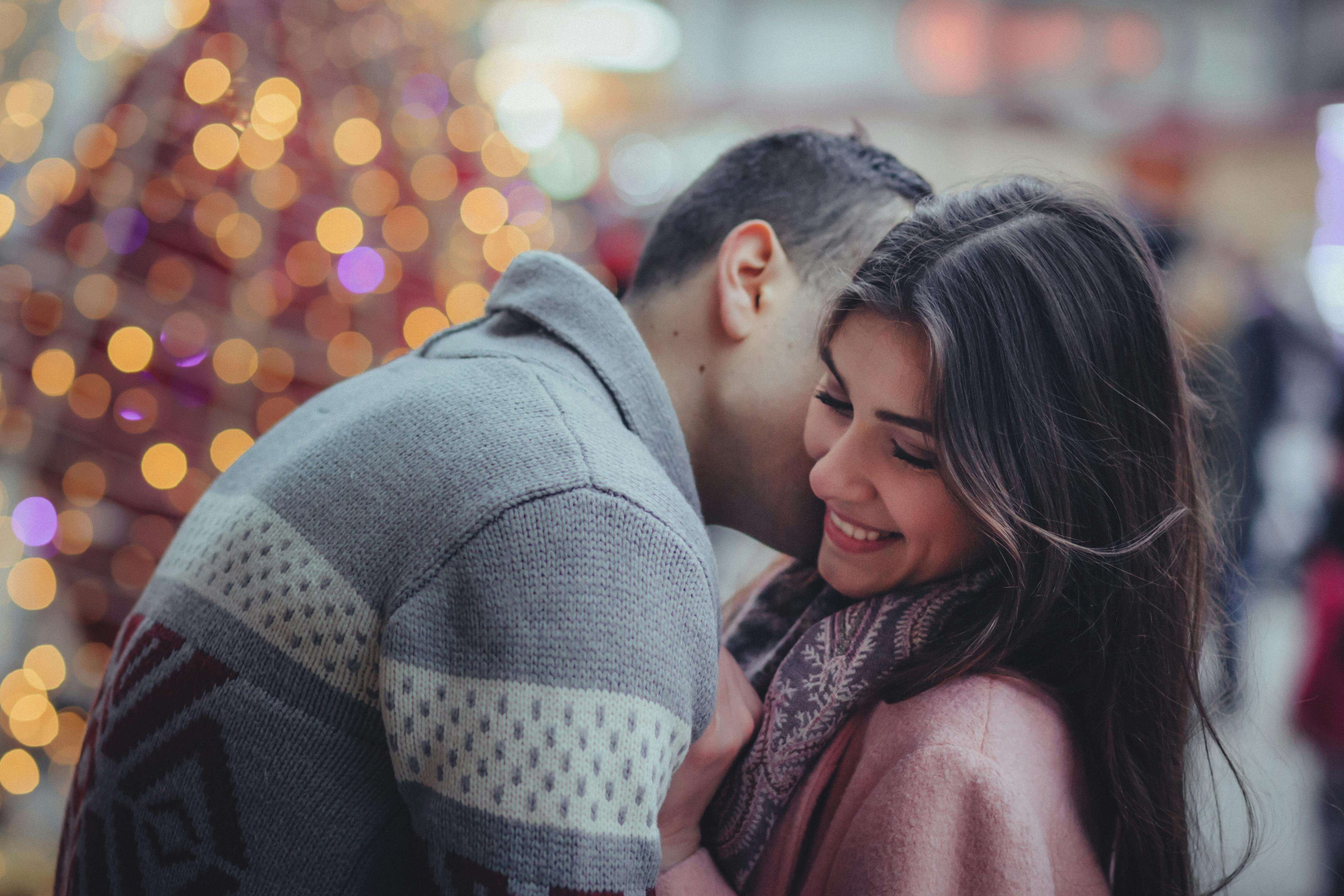 A couple sharing a warm embrace during the winter season, surrounded by festive lights.