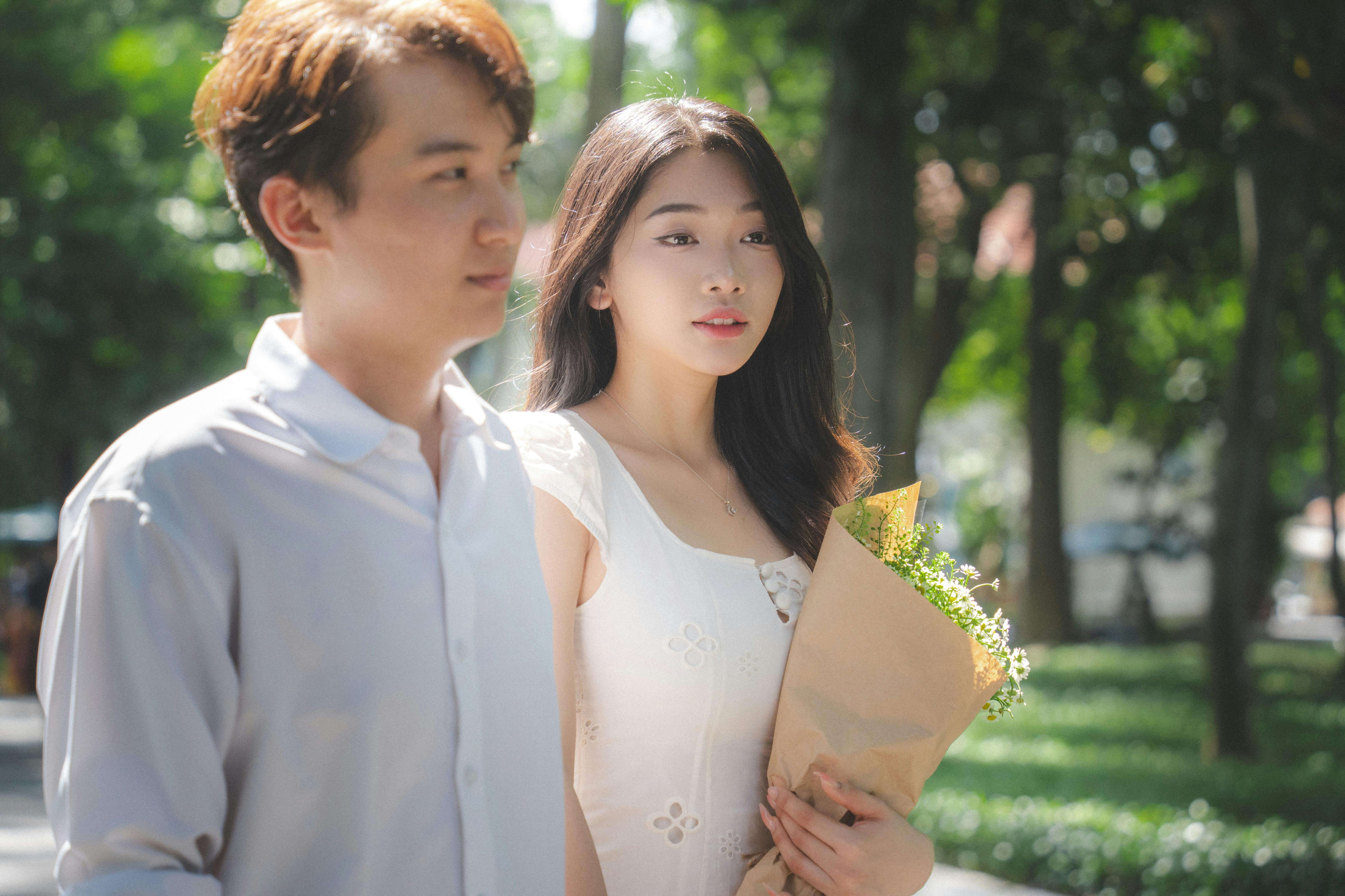 A young couple walking in a sunlit park, enjoying a bright day with flowers.