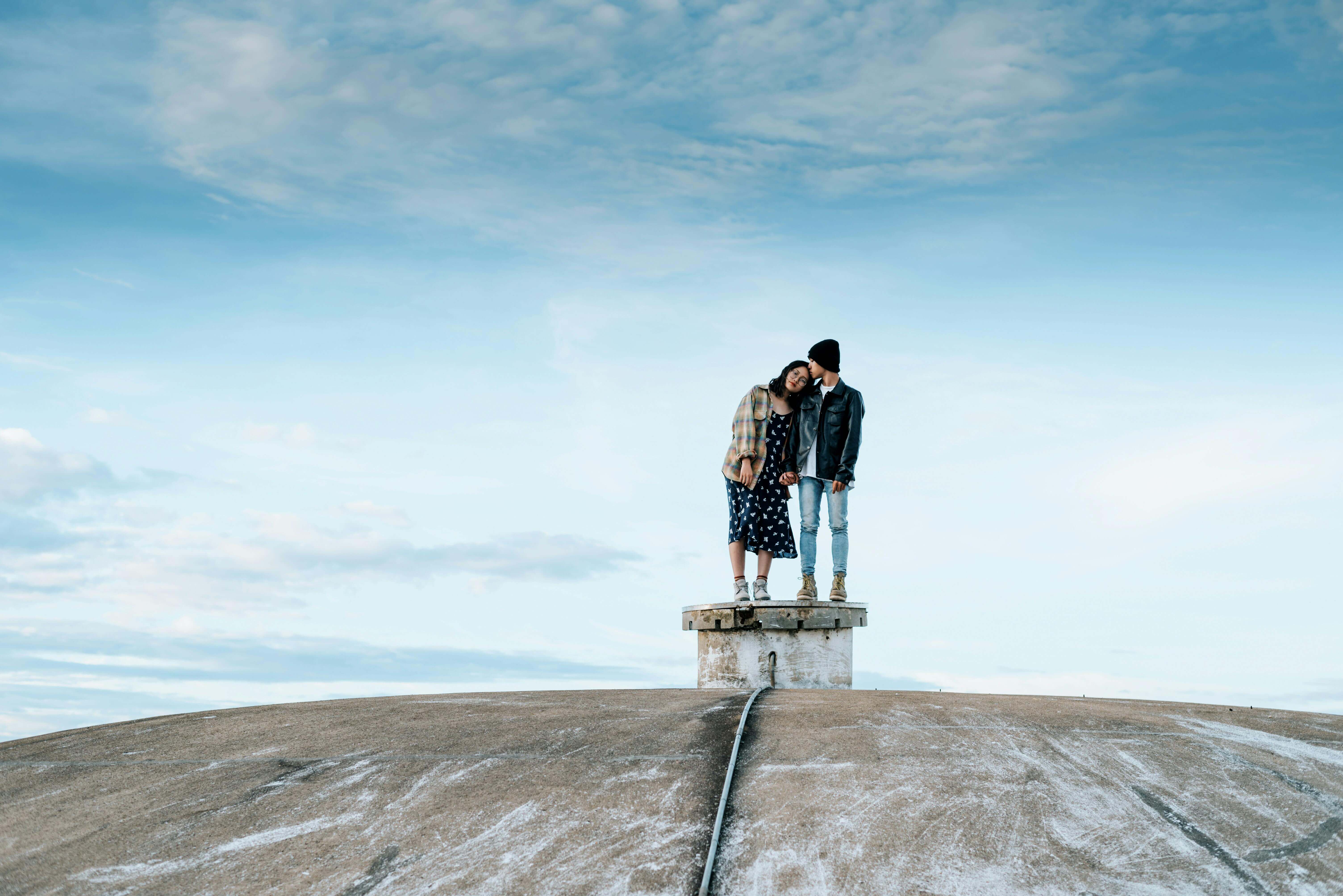 Young couple standing on a rooftop under blue skies, embracing love and freedom.