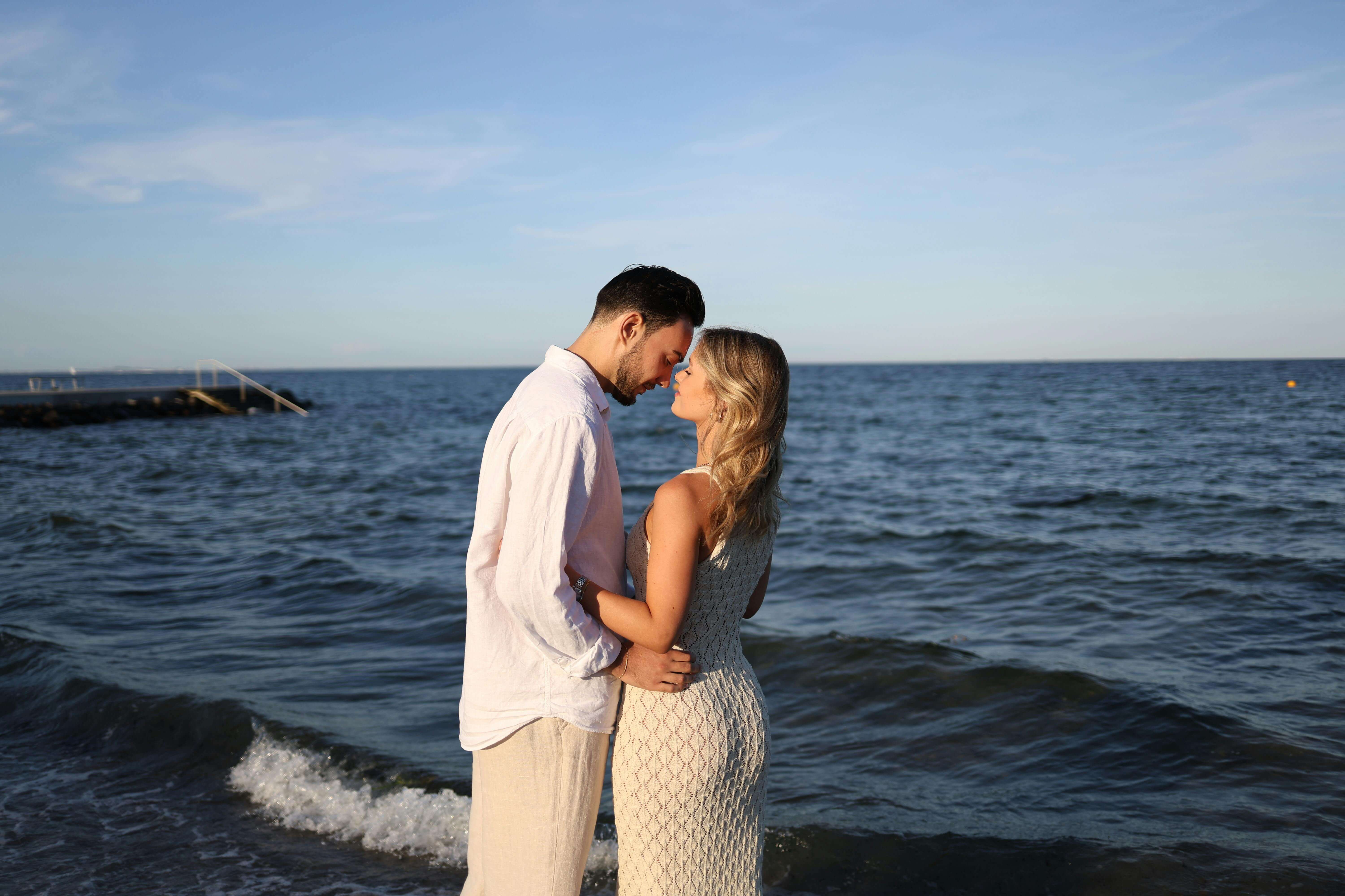 Couple embracing by the sea, capturing a romantic moment during sunset with serene ocean waves in the backdrop.