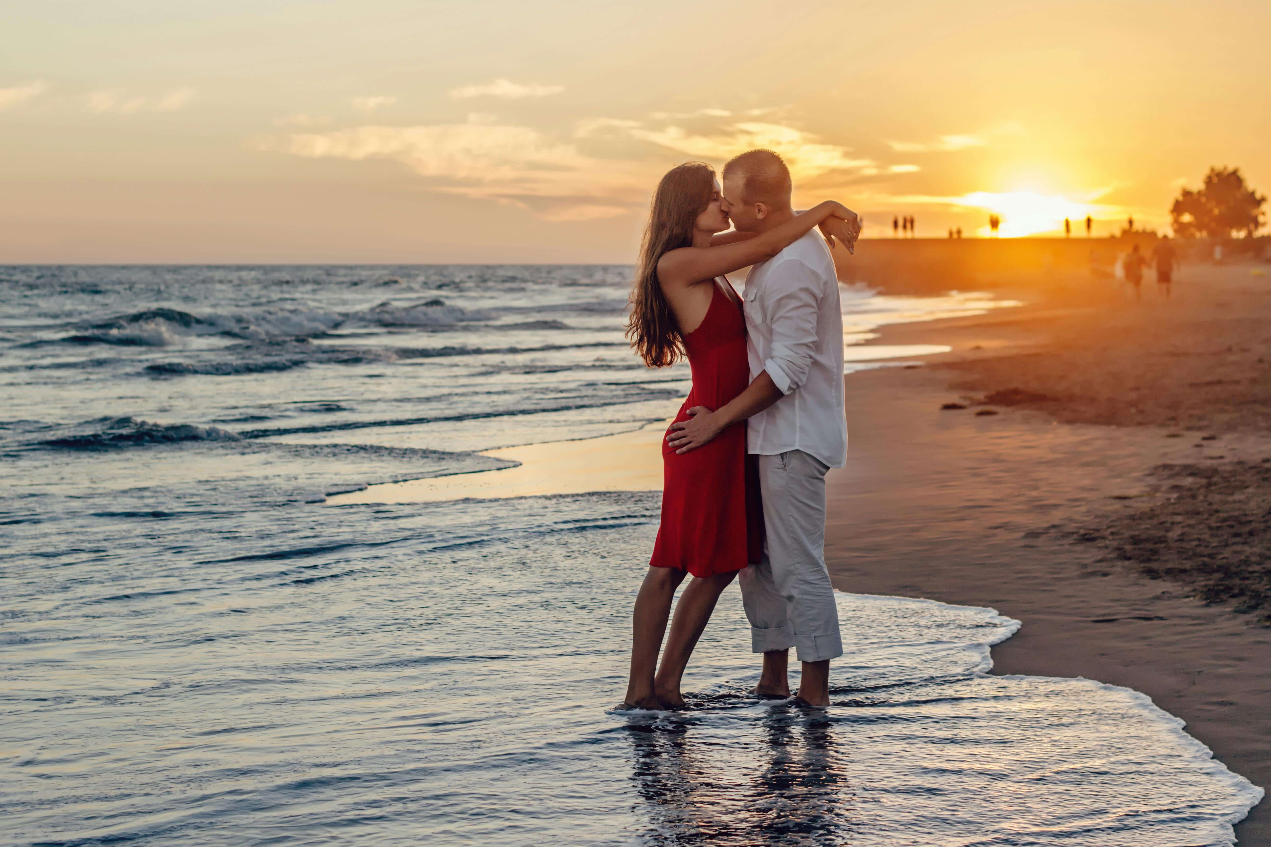 A couple in love embraces at the seaside during a vibrant sunset.