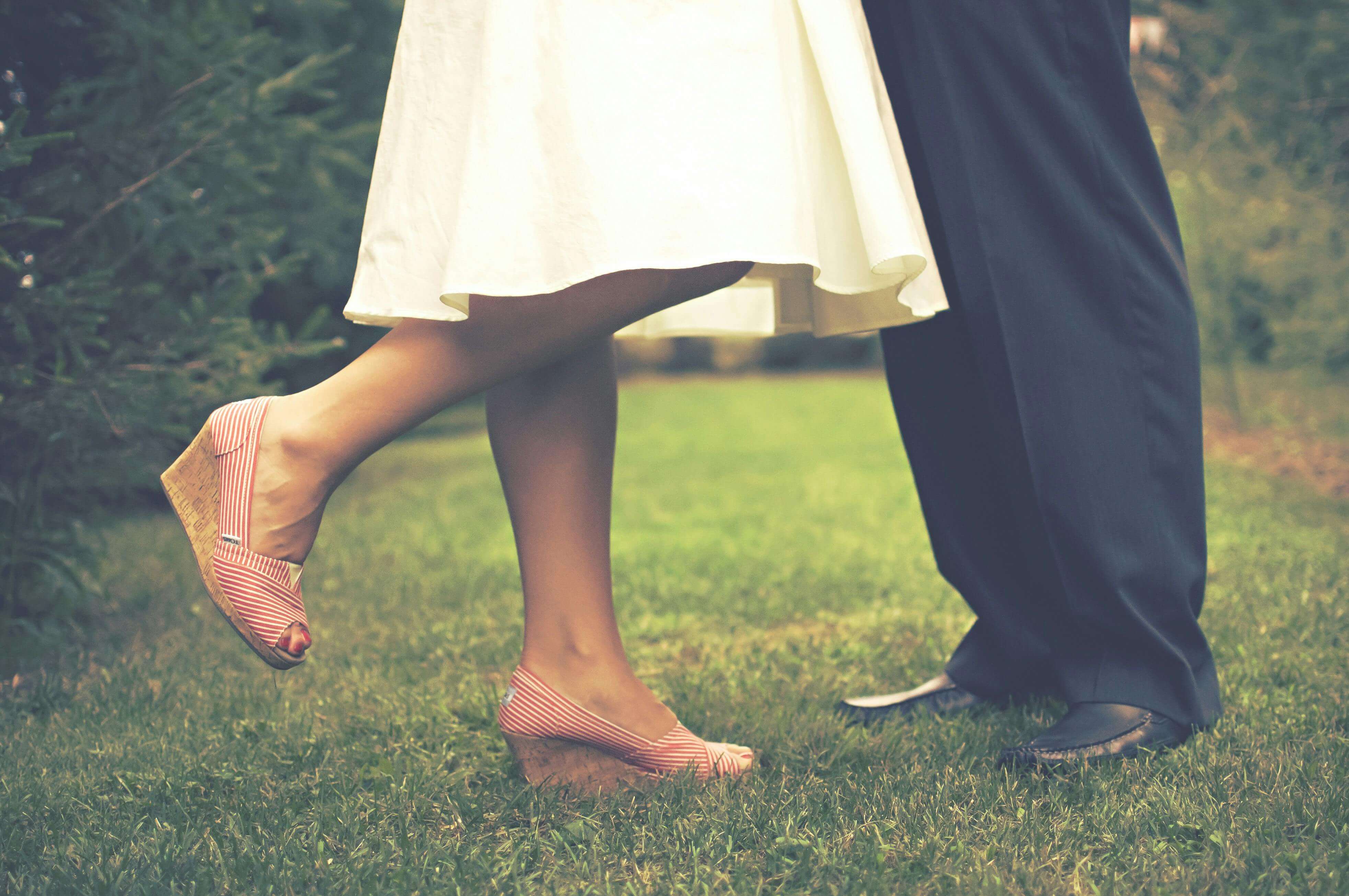 A couple's feet touching lovingly outdoors on grass, expressing romance.