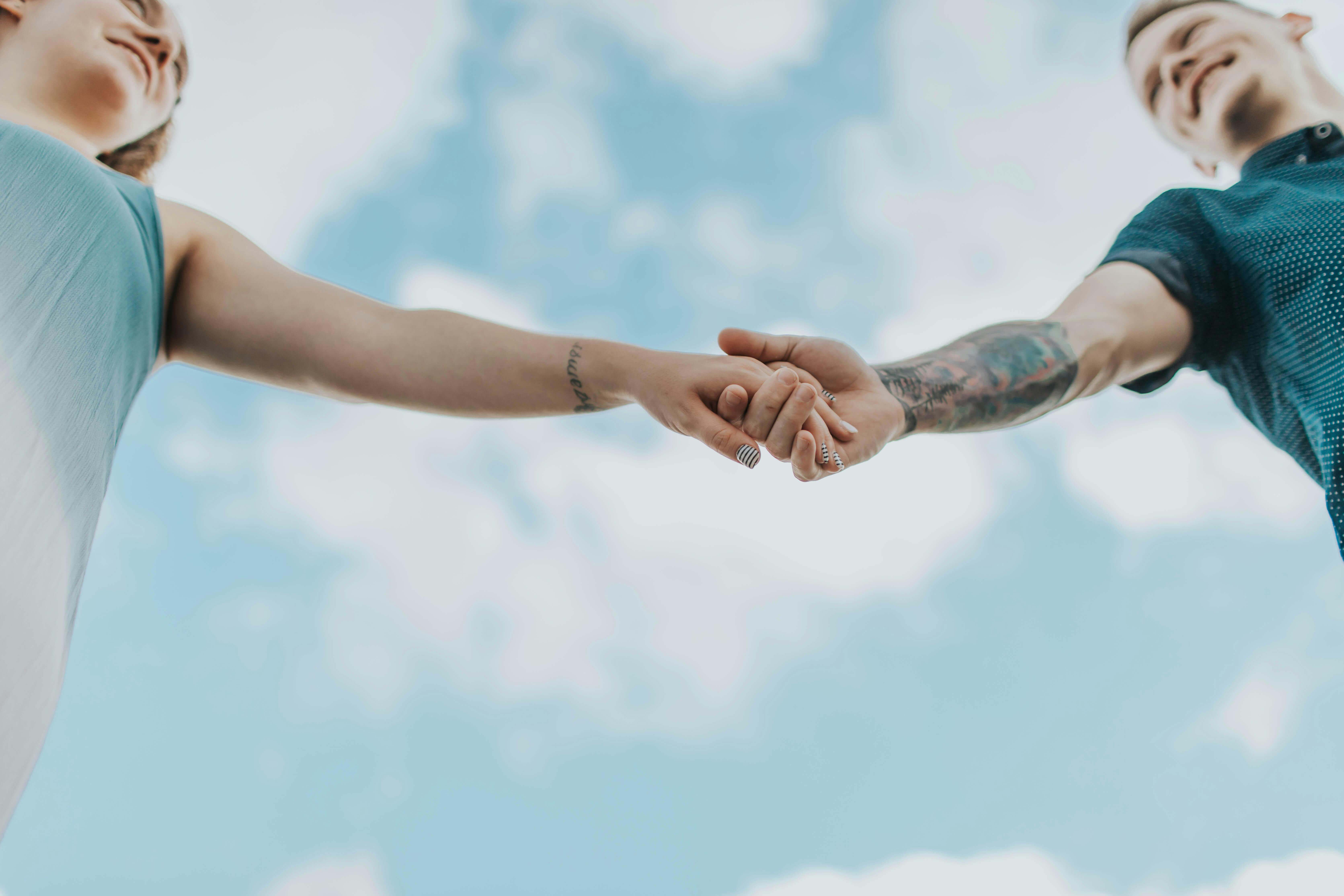 A couple holds hands outdoors, symbolizing love and connection, photographed from a low angle.