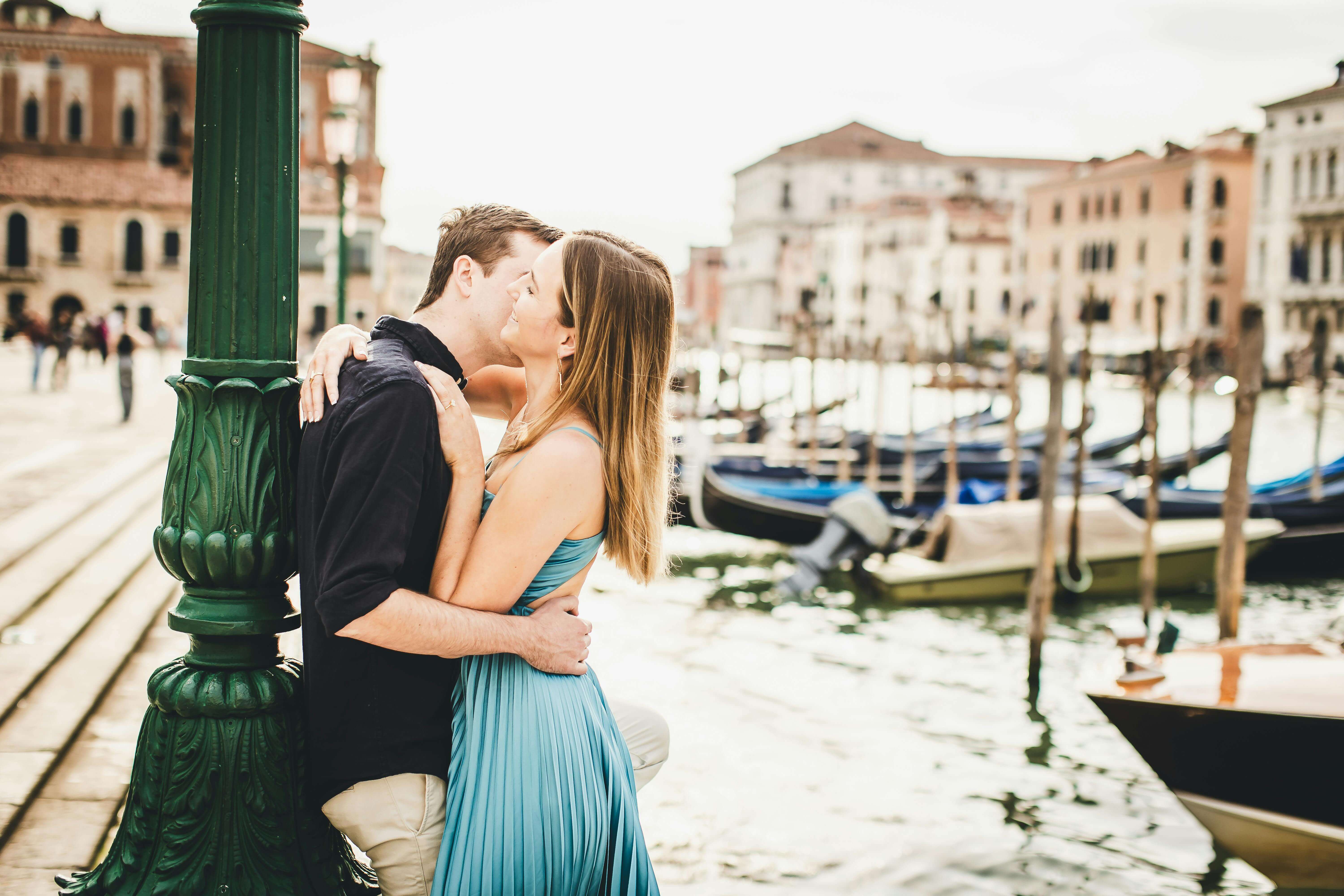 Couple sharing a kiss by the water in Venice, Italy's romantic setting.