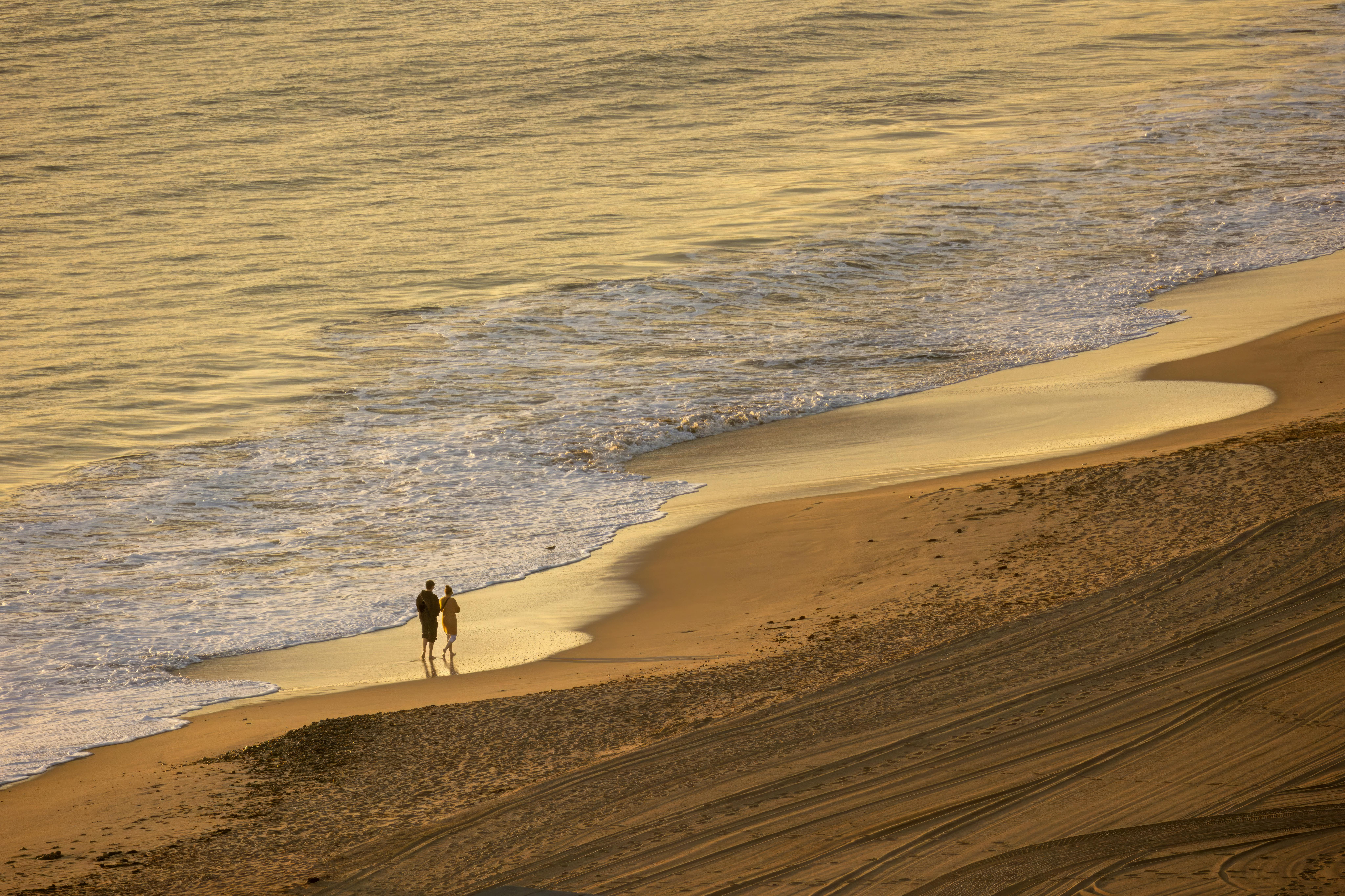 A couple strolls along a tranquil beach with gentle waves at sunset creating a romantic ambiance.