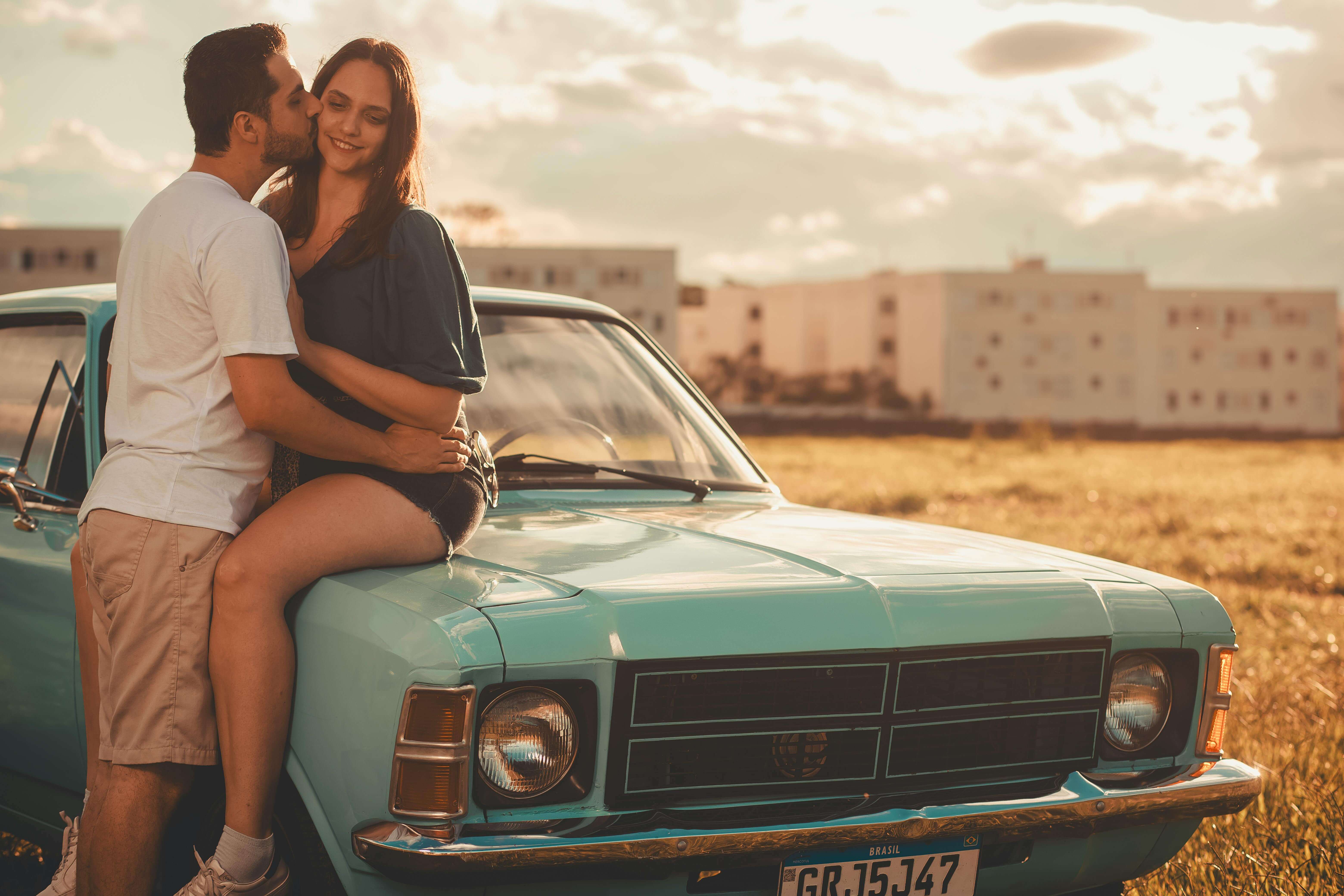 Romantic moment with couple on a vintage car in a sunny field