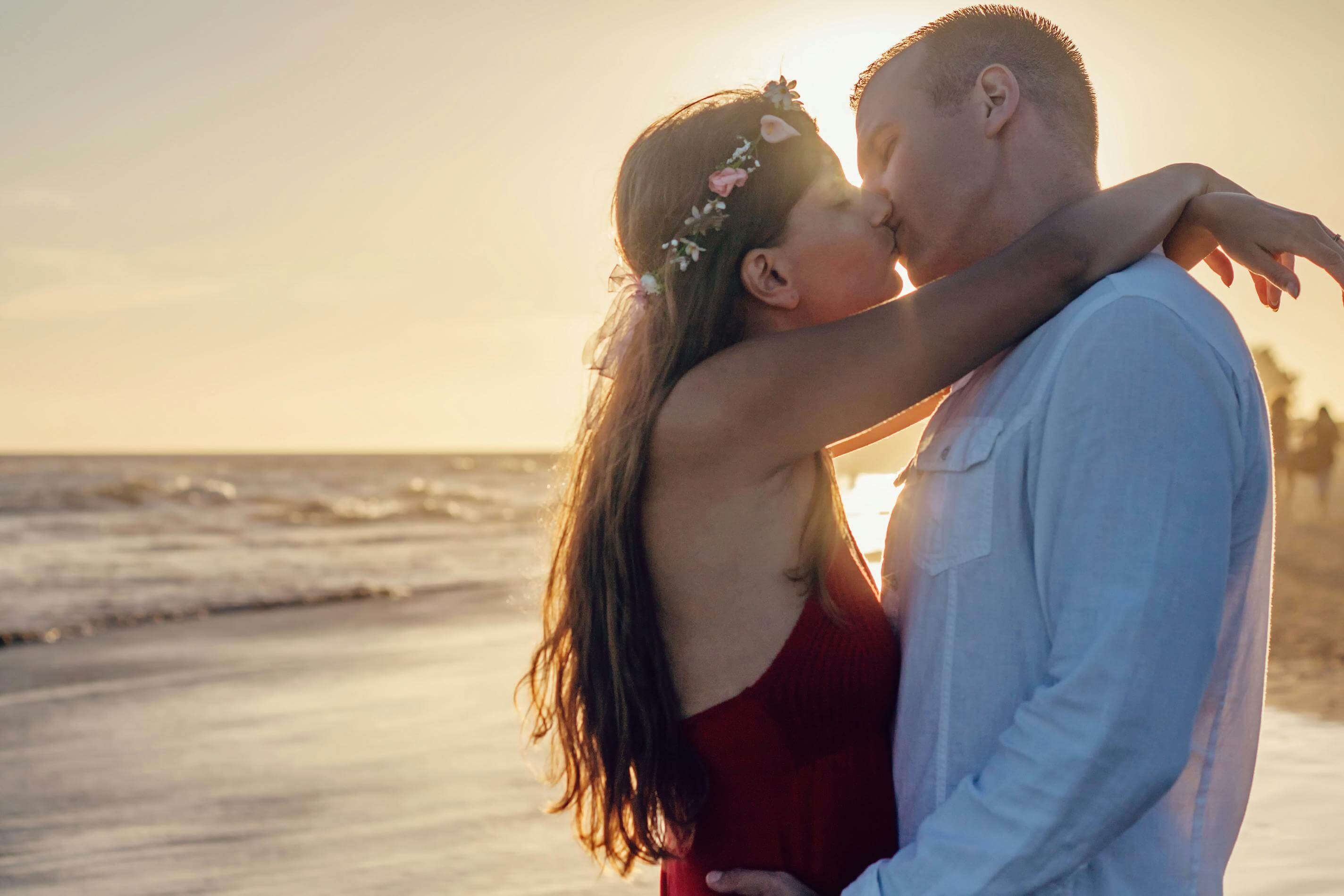 Young couple sharing a romantic kiss on a beach at sunset.