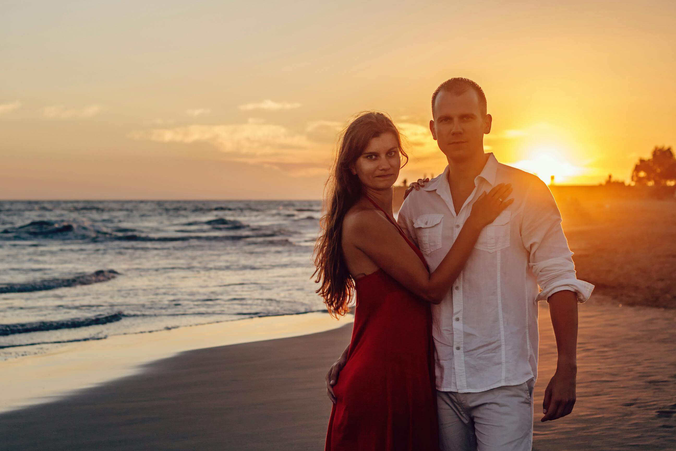 A couple embracing on a beach during a vibrant sunset, epitomizing romance and summer love.