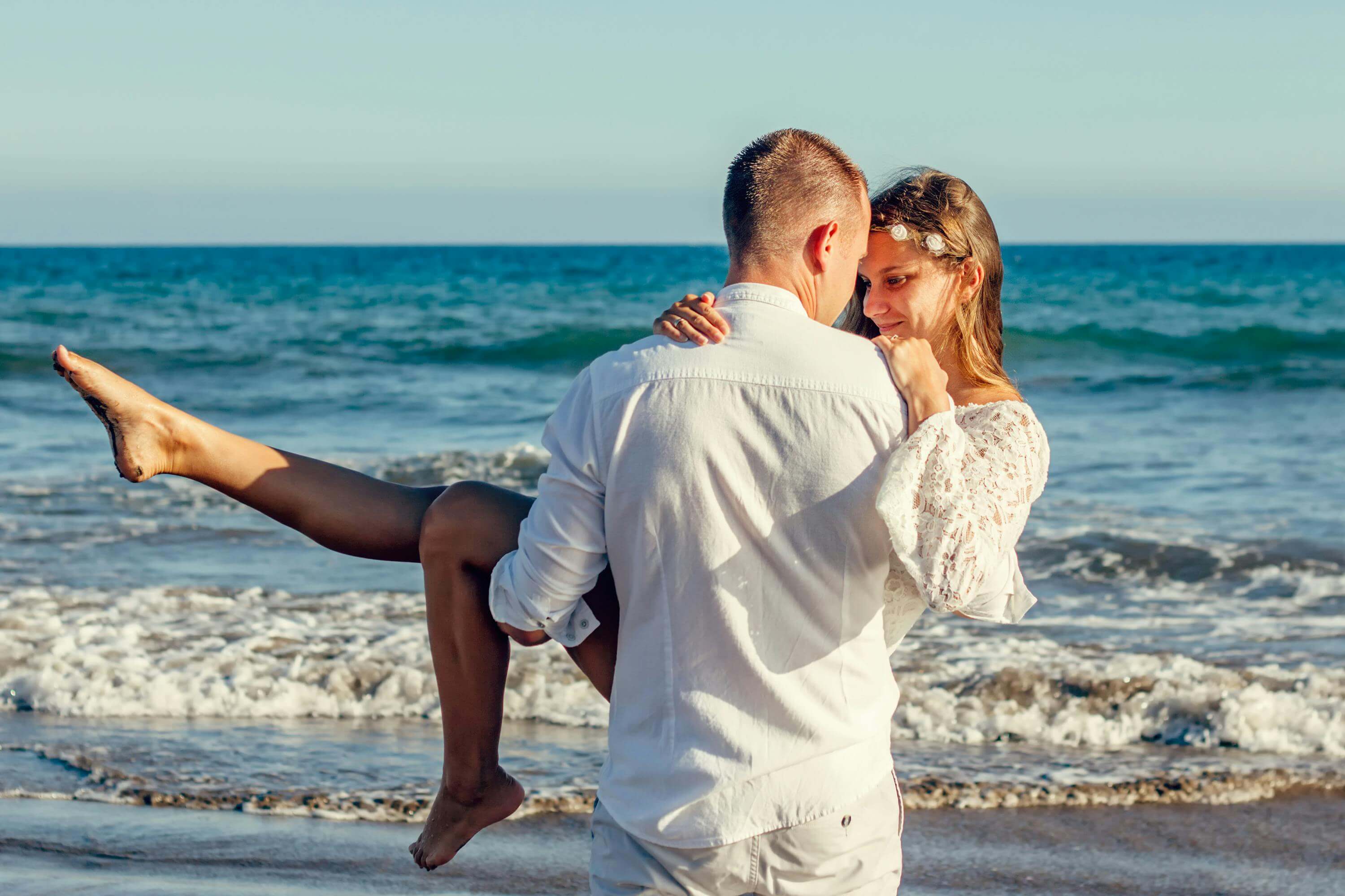 Young couple enjoying a romantic moment on a sunny beach, with waves in the background.