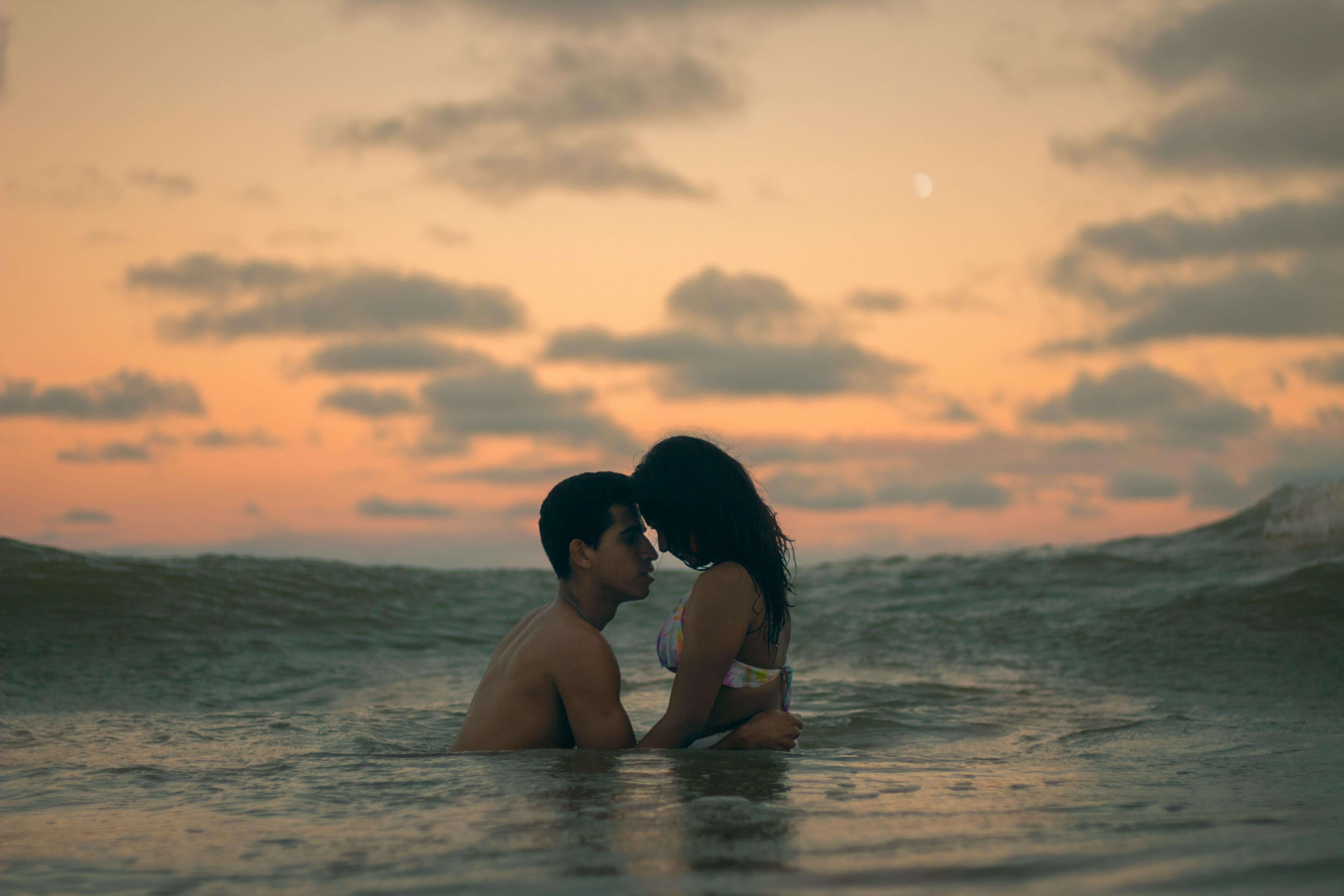 A couple embraces in the ocean during a romantic sunset, capturing love and intimacy.