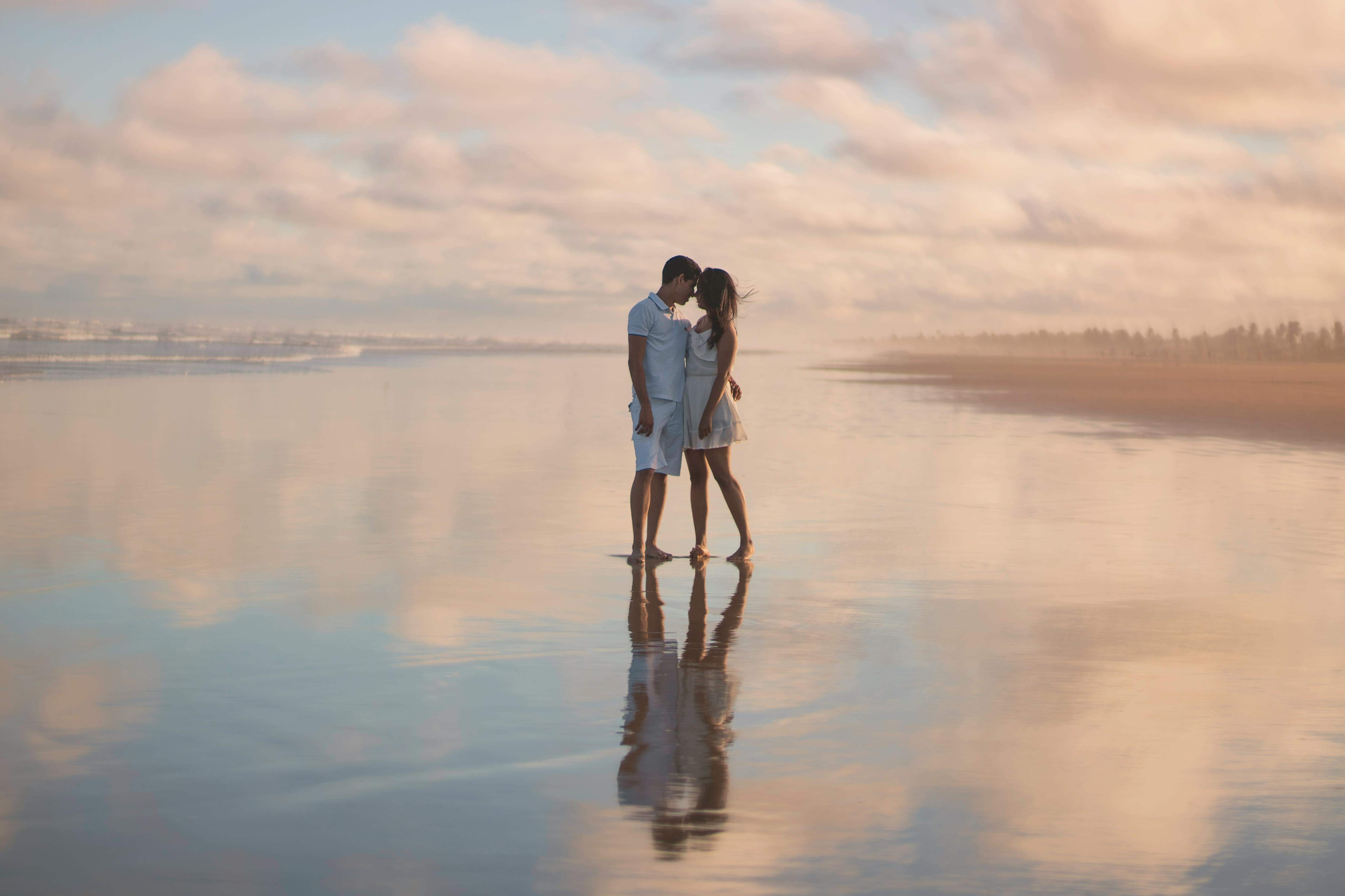 A couple embraces on a serene beach during sunset, reflecting on wet sand.