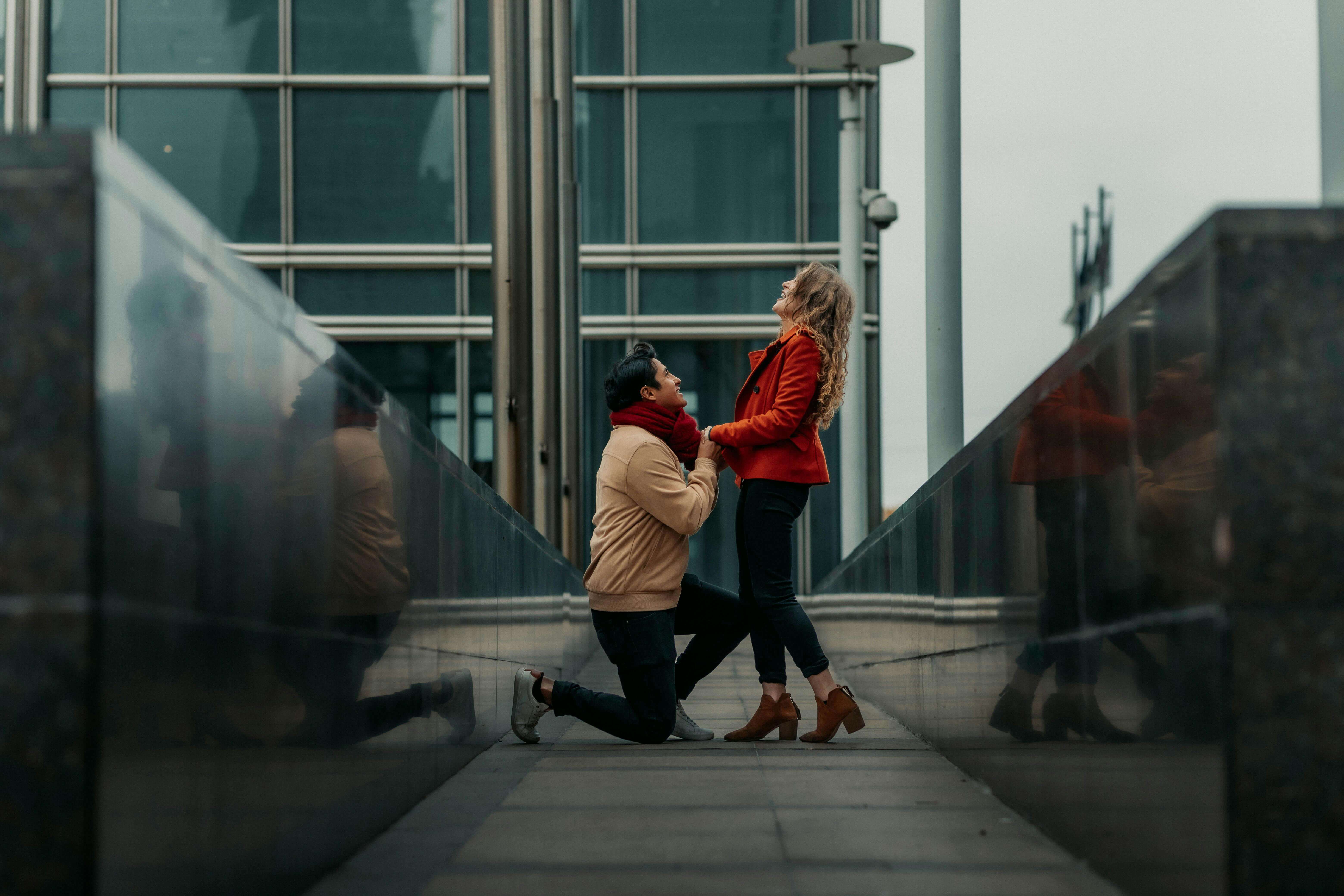 A man romantically proposes to a woman outdoors in a modern city environment.