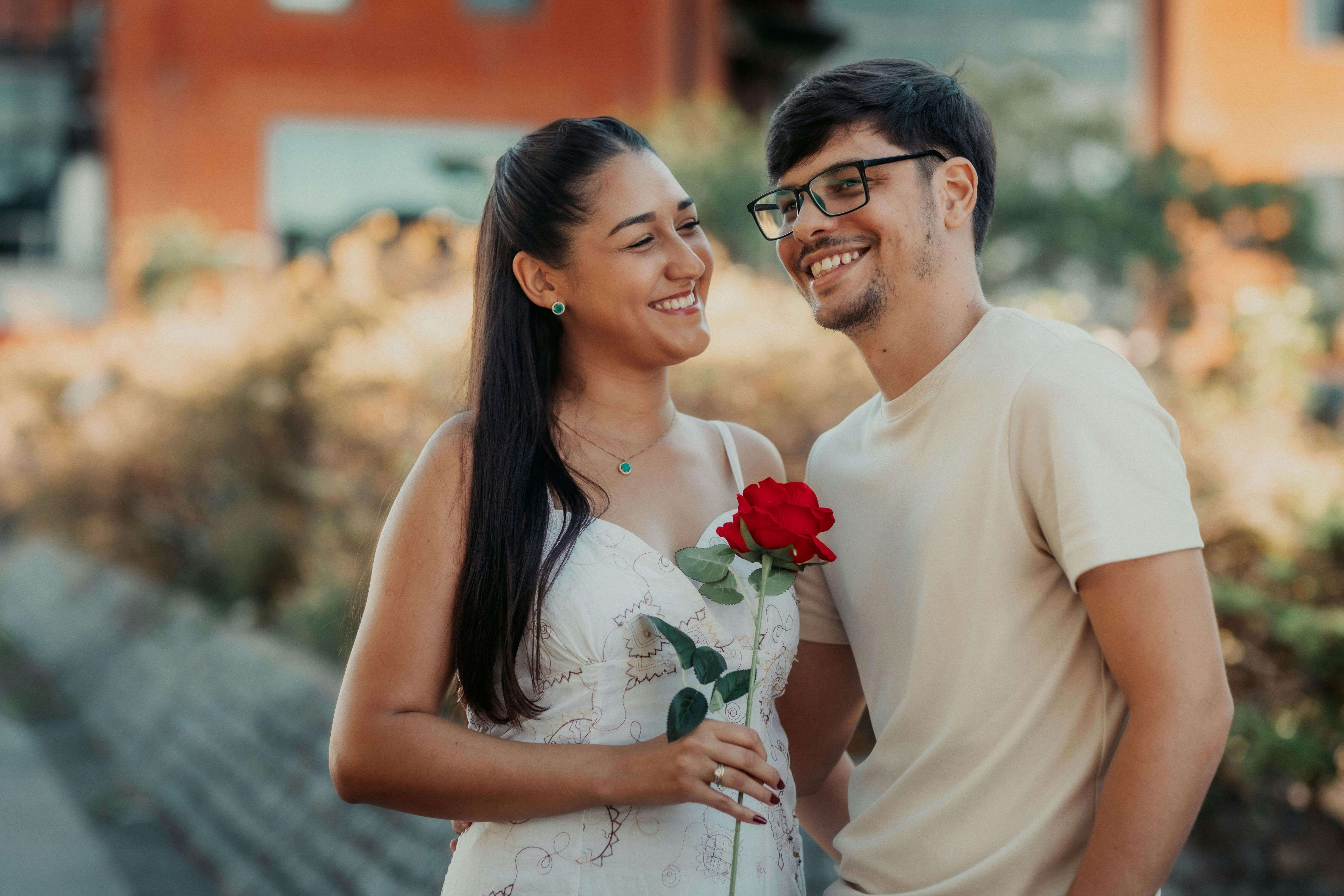 A young couple enjoying a romantic moment outdoors, exchanging smiles and a rose.