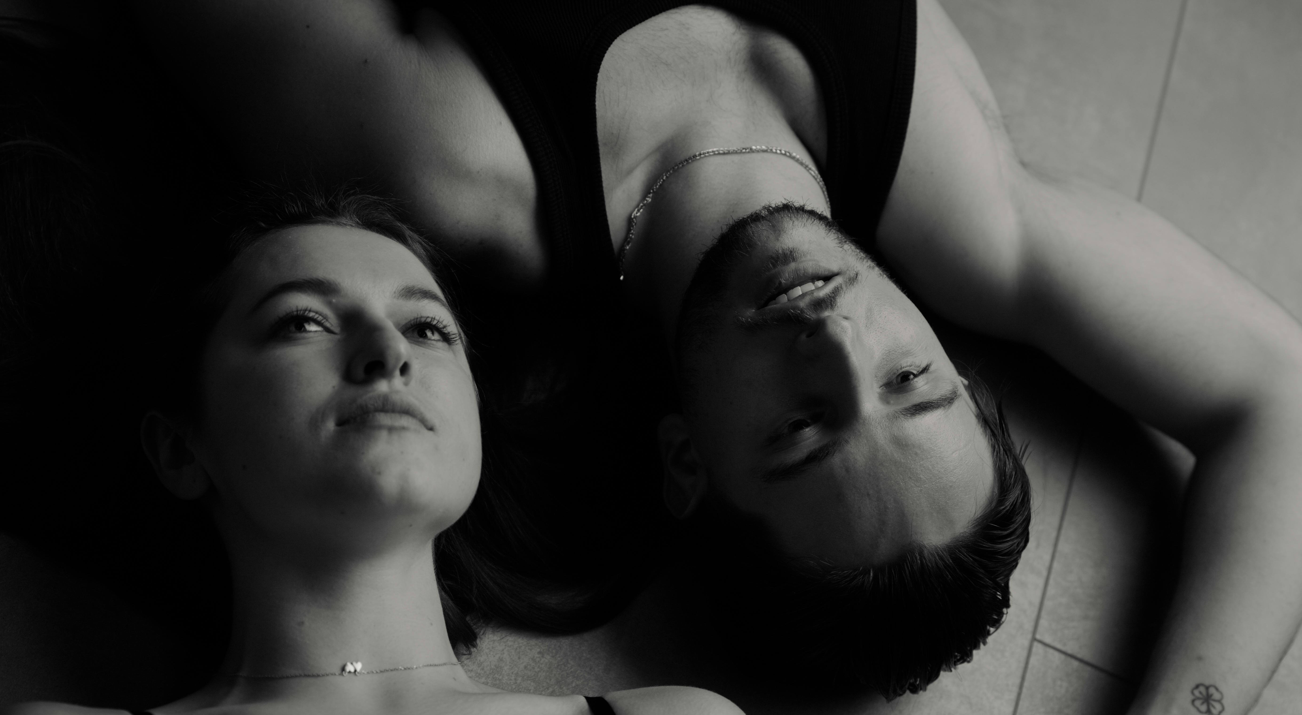 Intimate black and white portrait of a couple lying on the floor, expressing tenderness and serenity.