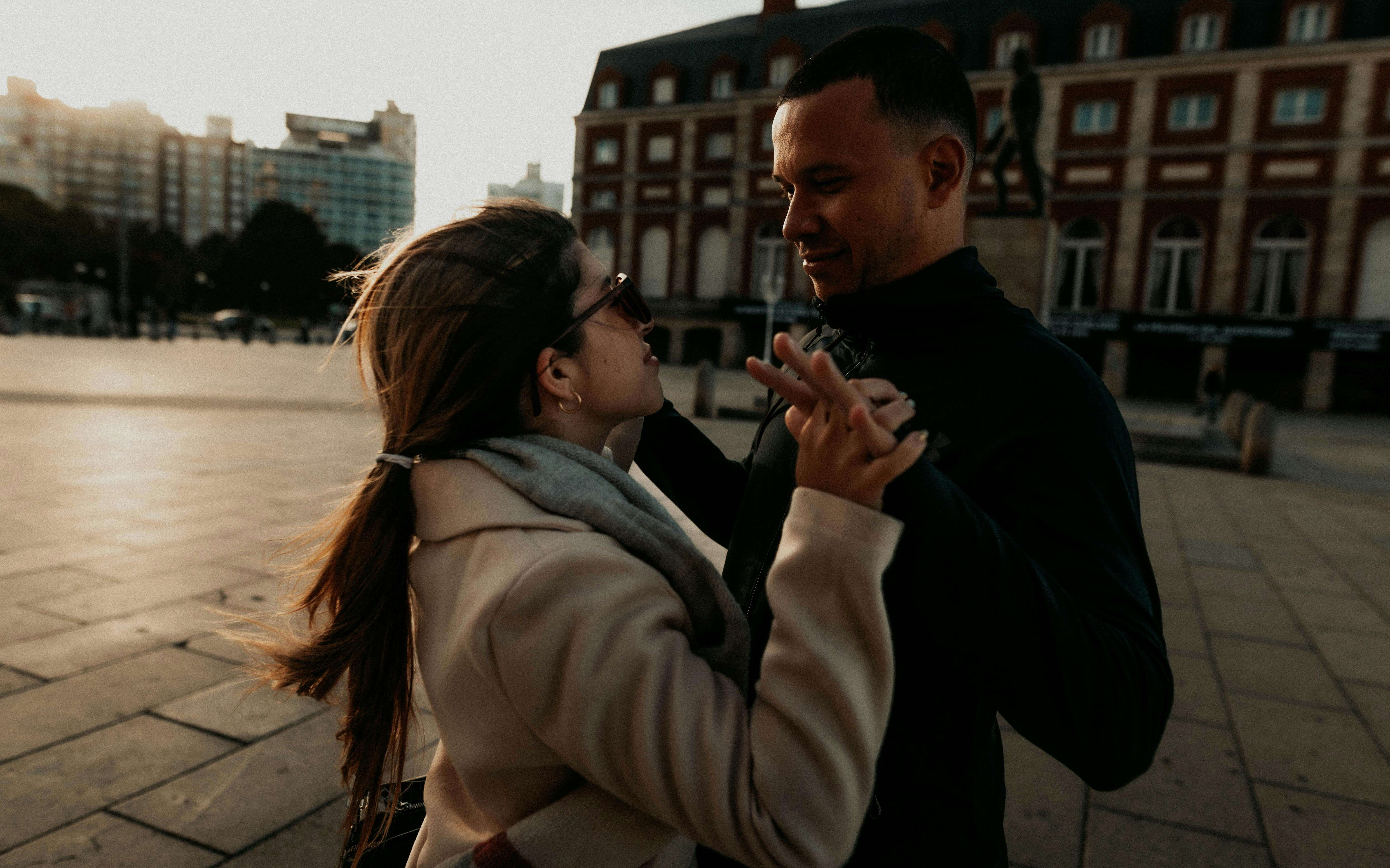 Romantic couple dancing joyfully outdoors in an urban setting at dusk.
