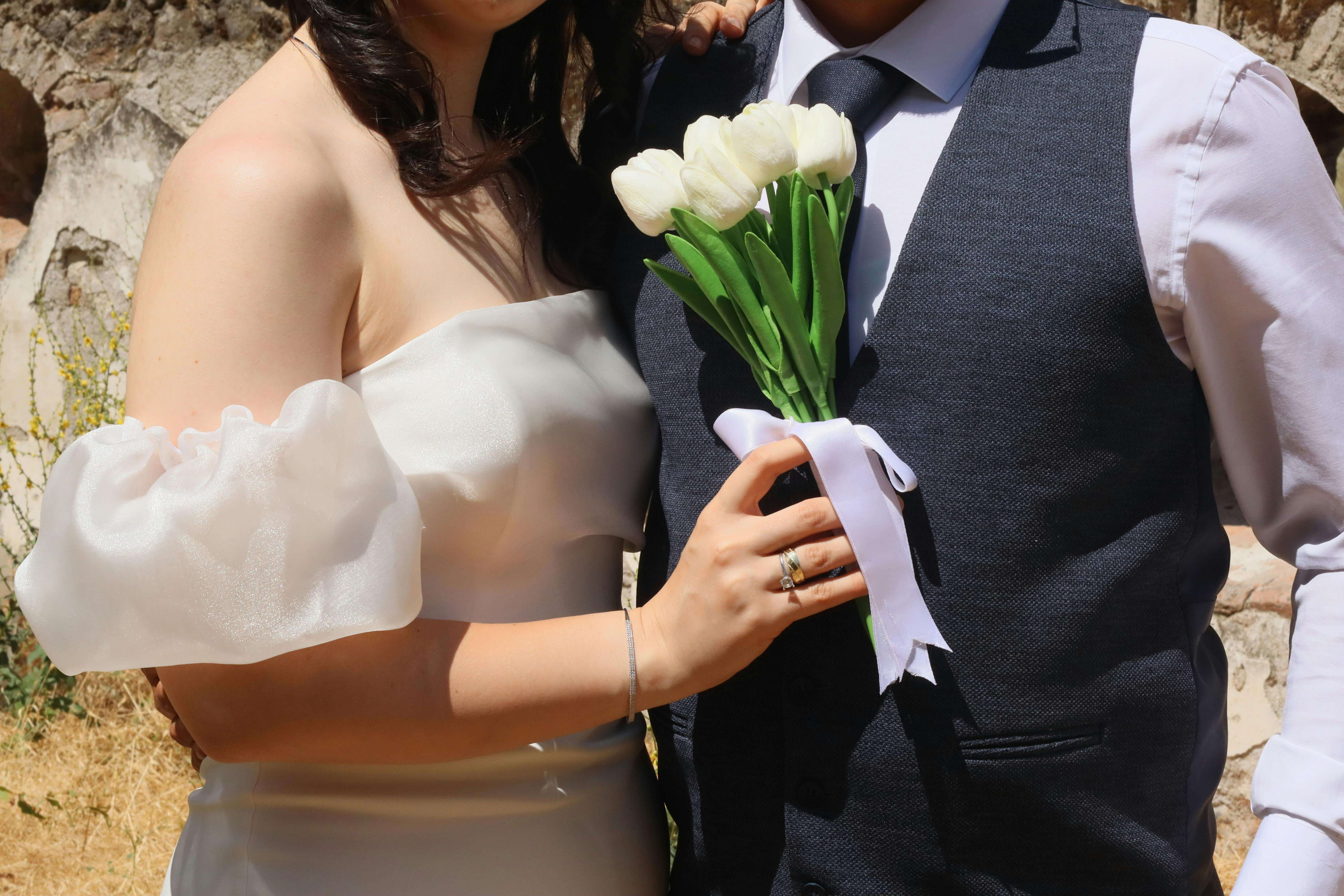 A close-up shot of a wedding couple holding white tulips in an outdoor setting.