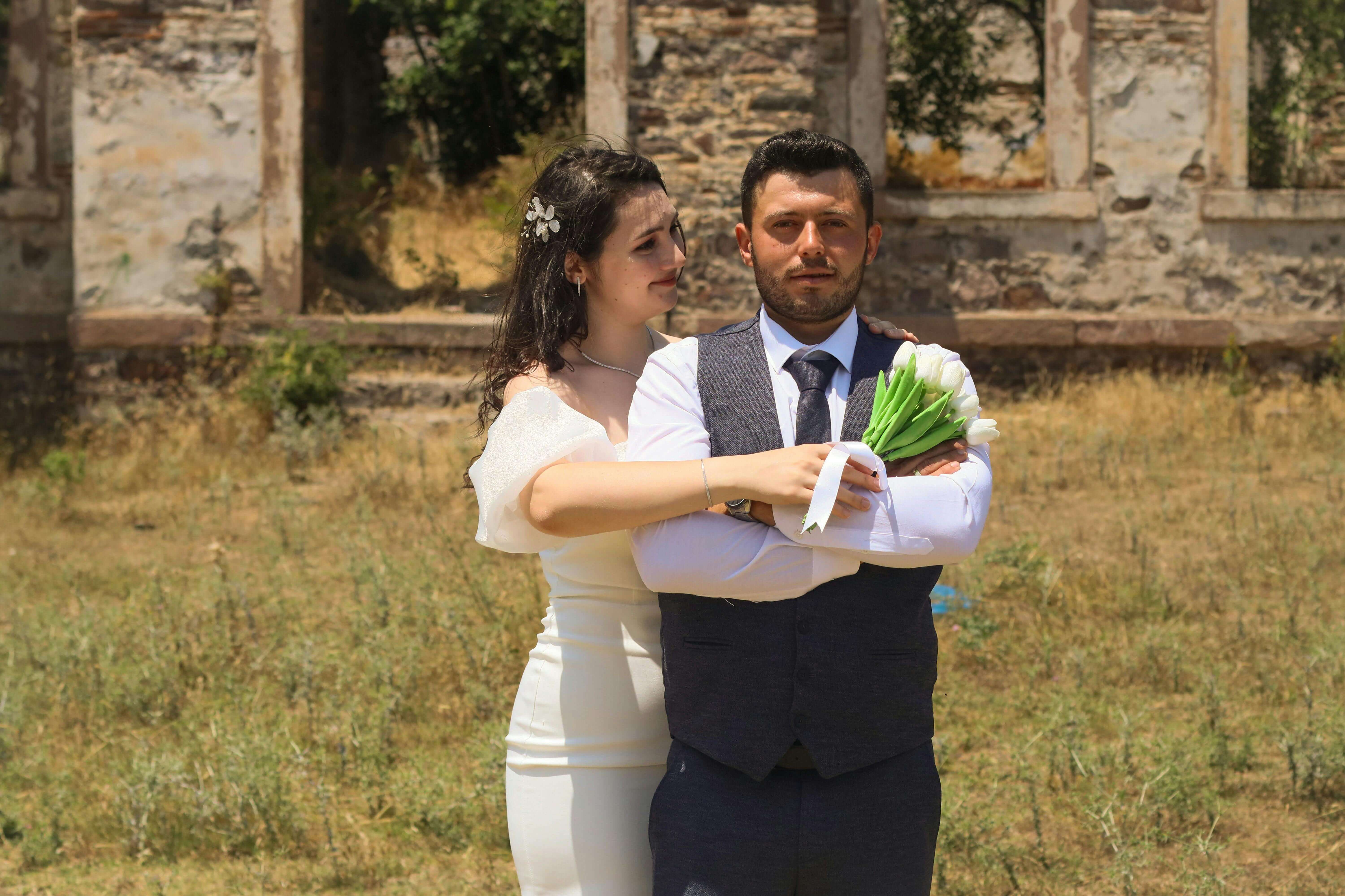 Bride and groom pose in rustic outdoor setting, exuding love and elegance.