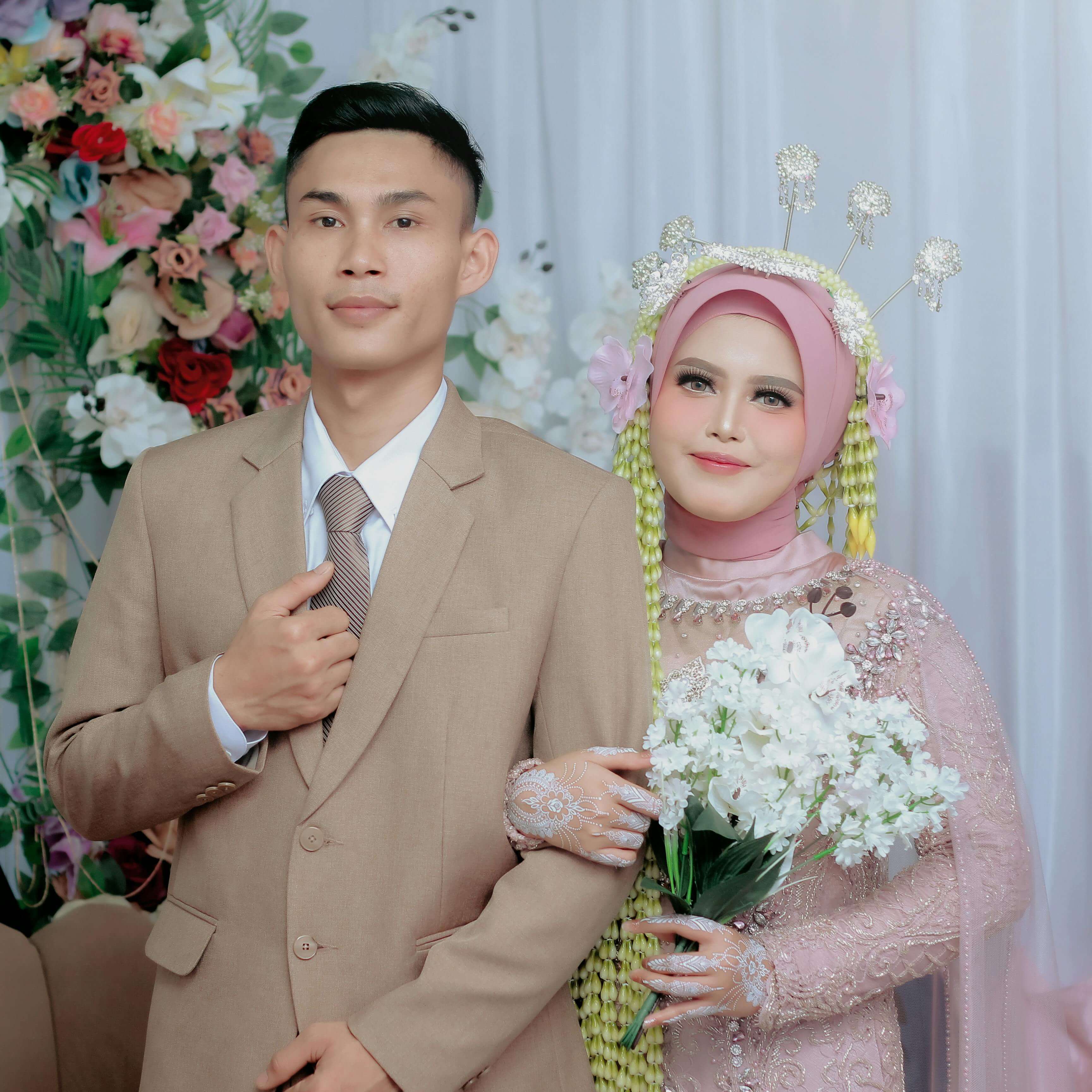 A joyful newlywed couple posing elegantly with flowers and traditional attire.