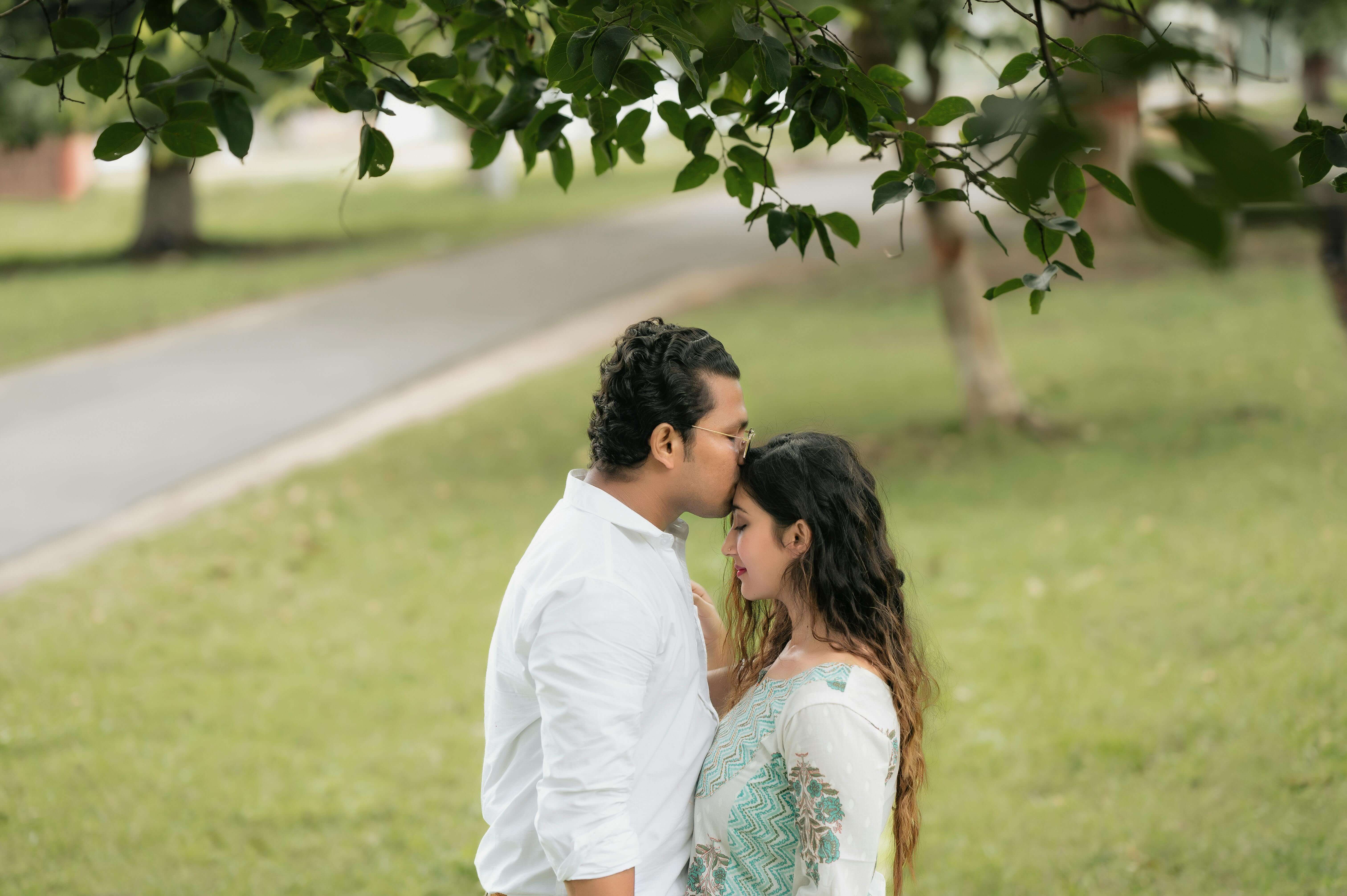 A tender moment shared by a couple in a lush, green park under a tree.