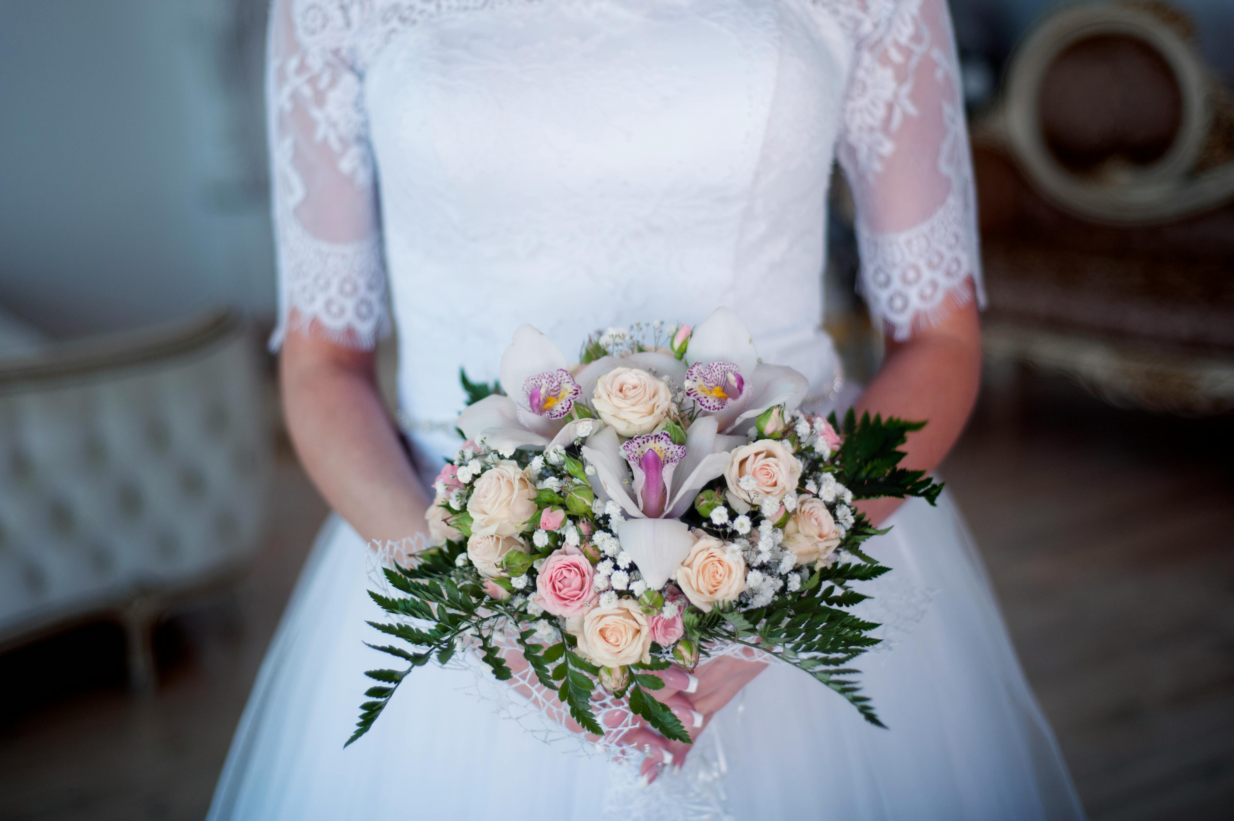 Close-up of a bride holding a delicate bouquet with white and pink flowers in a lace wedding dress.