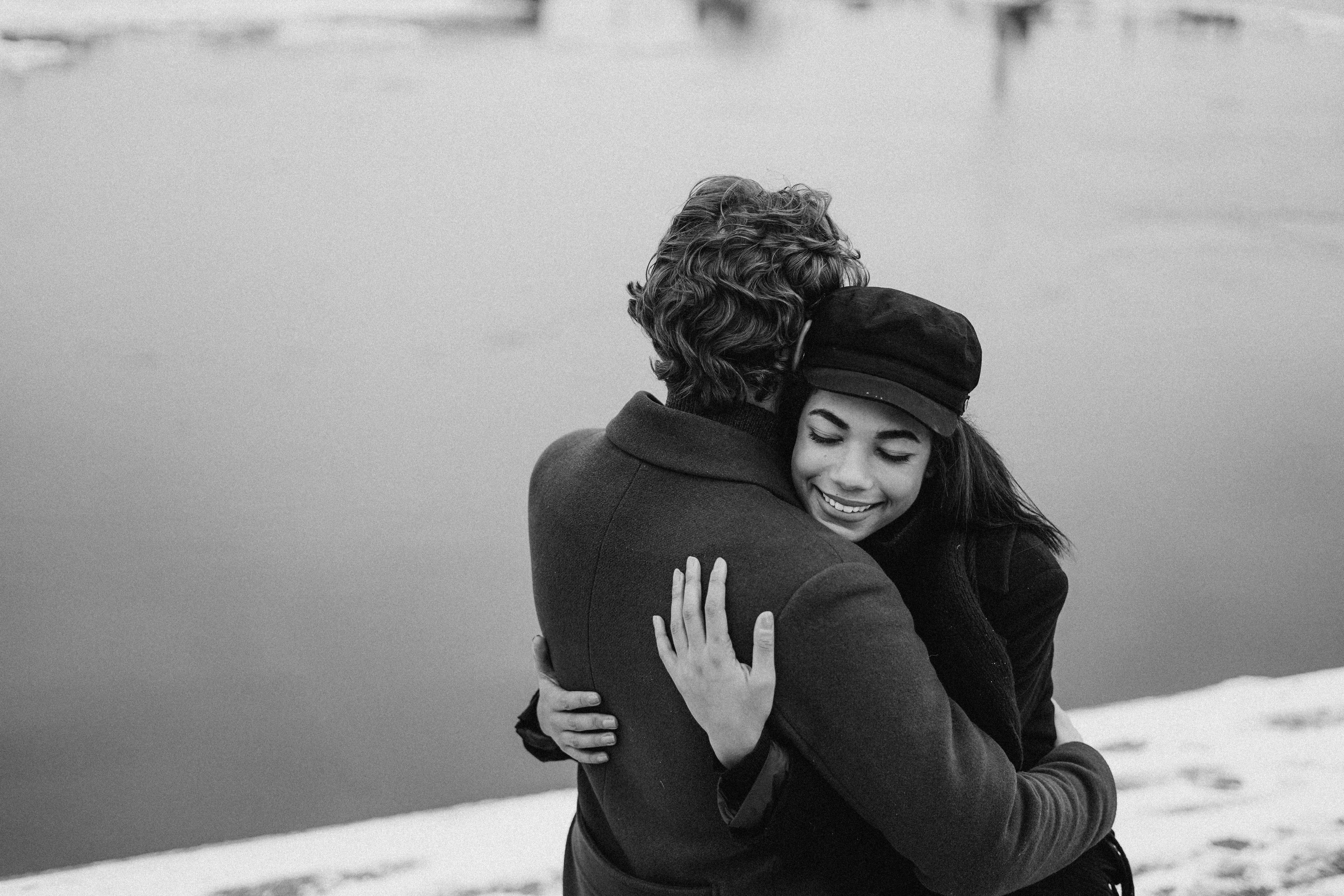 A couple sharing a warm embrace by the snowy lakeside, showcasing love and happiness.
