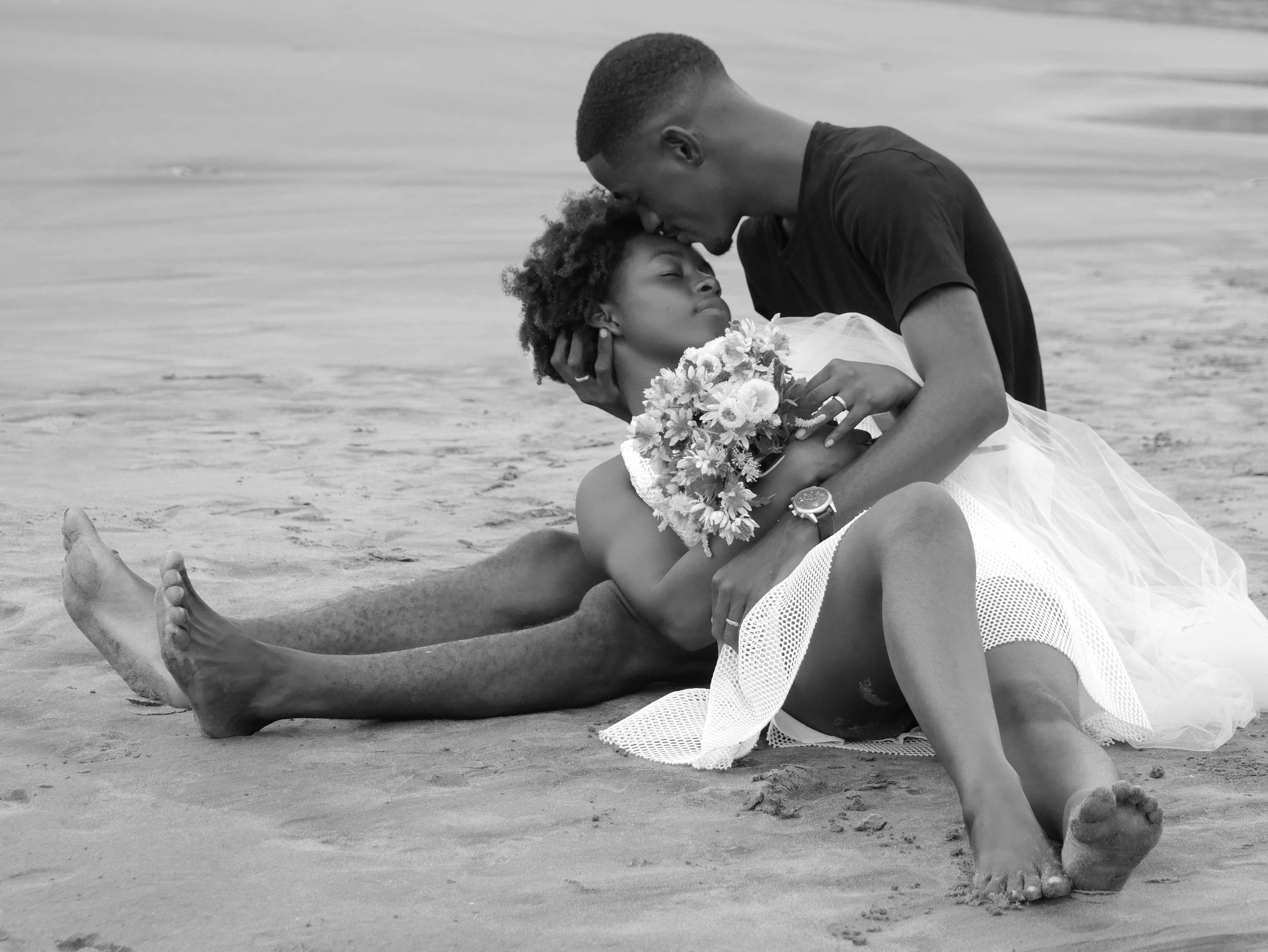 Black and white photo of a couple sharing a tender moment by the beach, expressing love and intimacy.