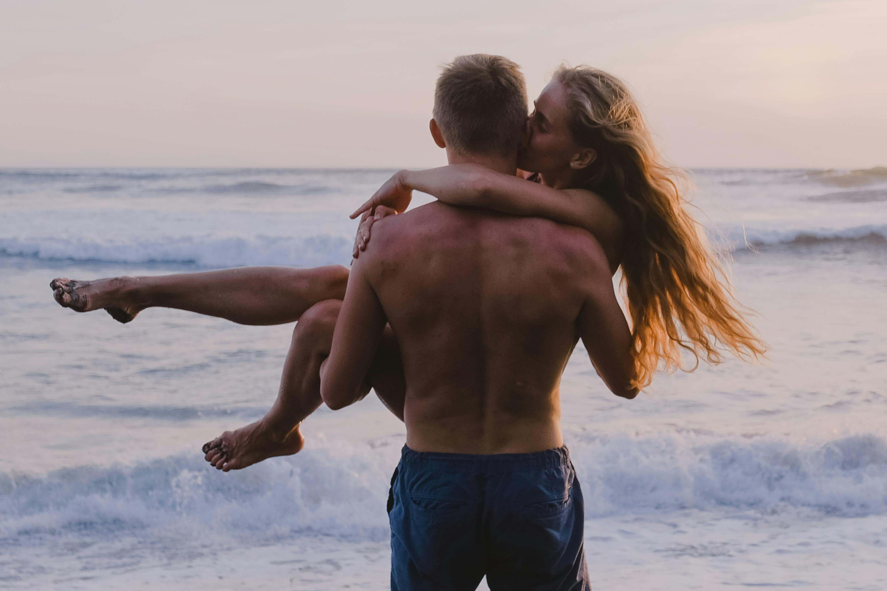 Romantic couple embracing at sunset on a beach, with waves crashing behind them.