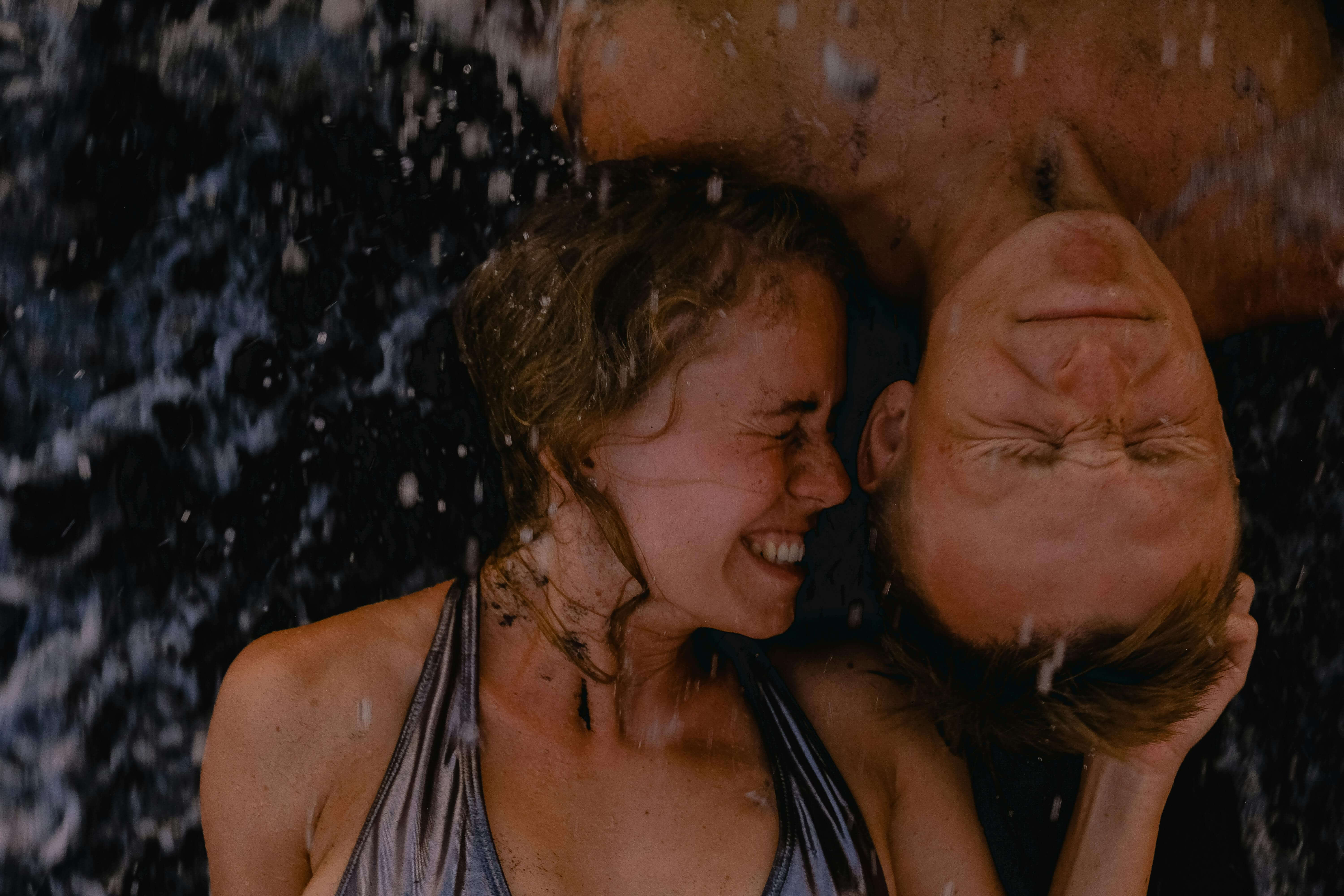 Joyful couple embracing beach waves, eyes closed, under summer sun.
