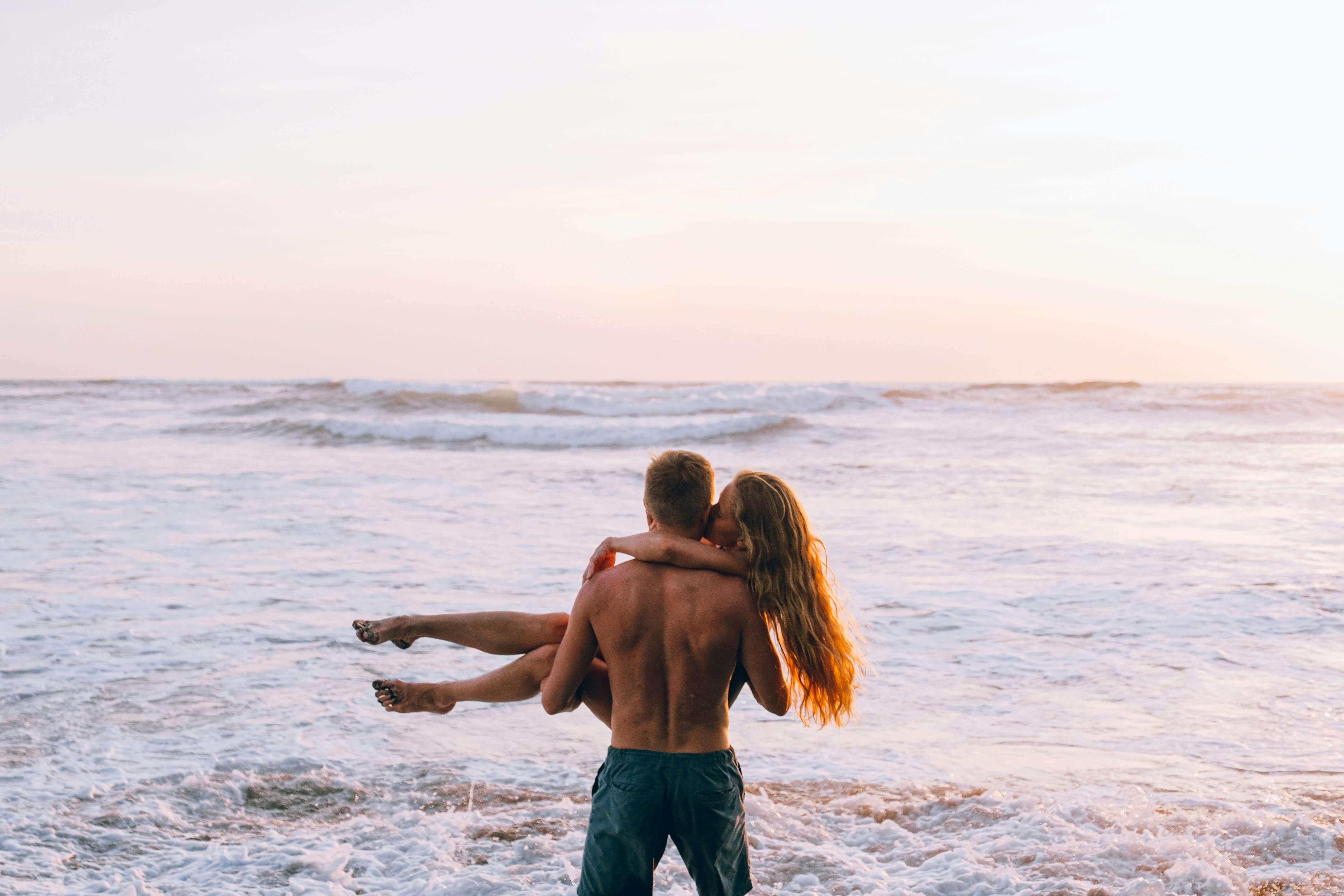 A couple in a loving embrace on a beach during sunset, symbolizing romance and tranquility.