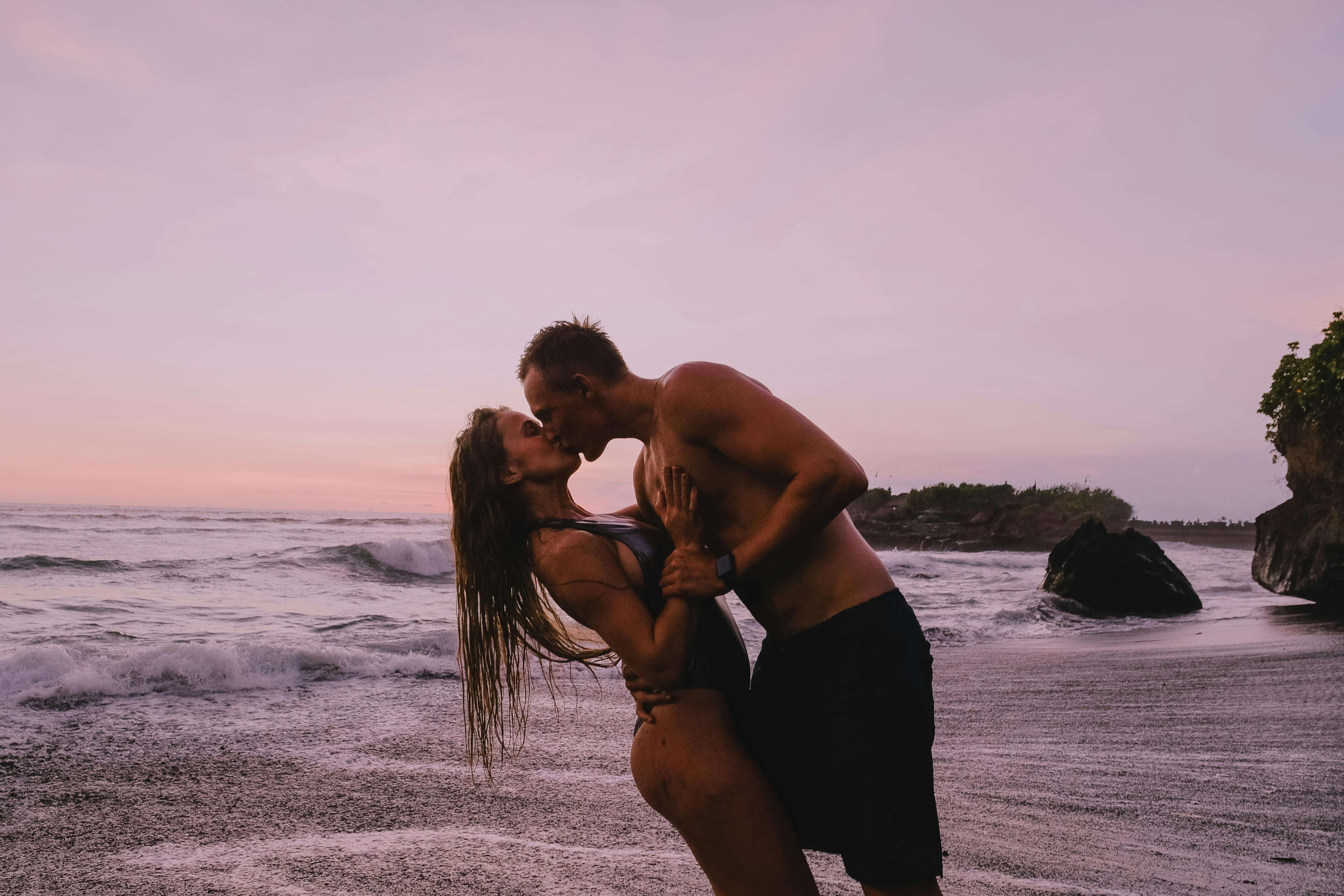 Couple sharing a romantic kiss on a beach at sunset, creating a warm and intimate moment.