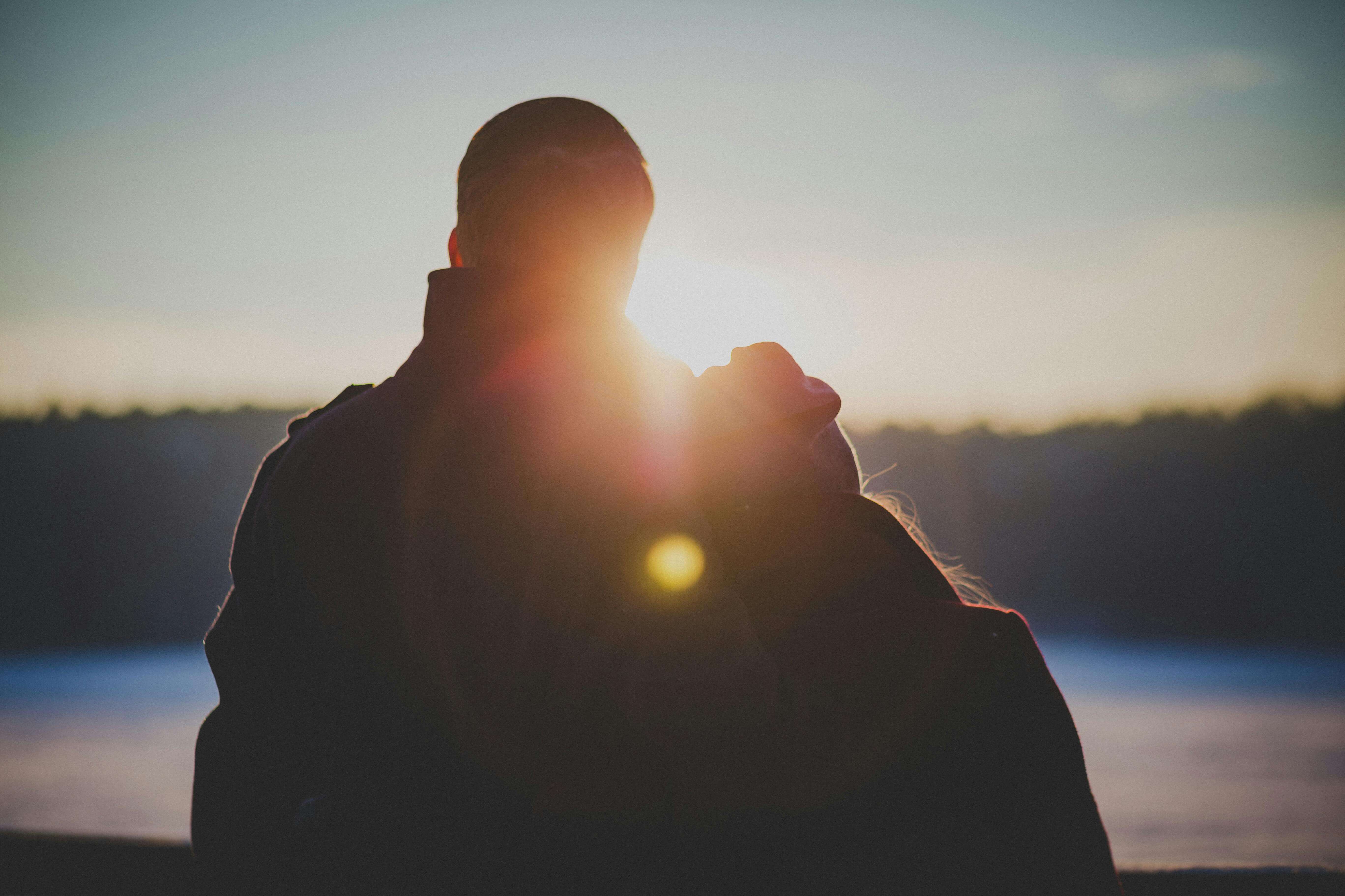A romantic couple embraces with a beautiful lens flare at sunrise, creating a warm and intimate silhouette.