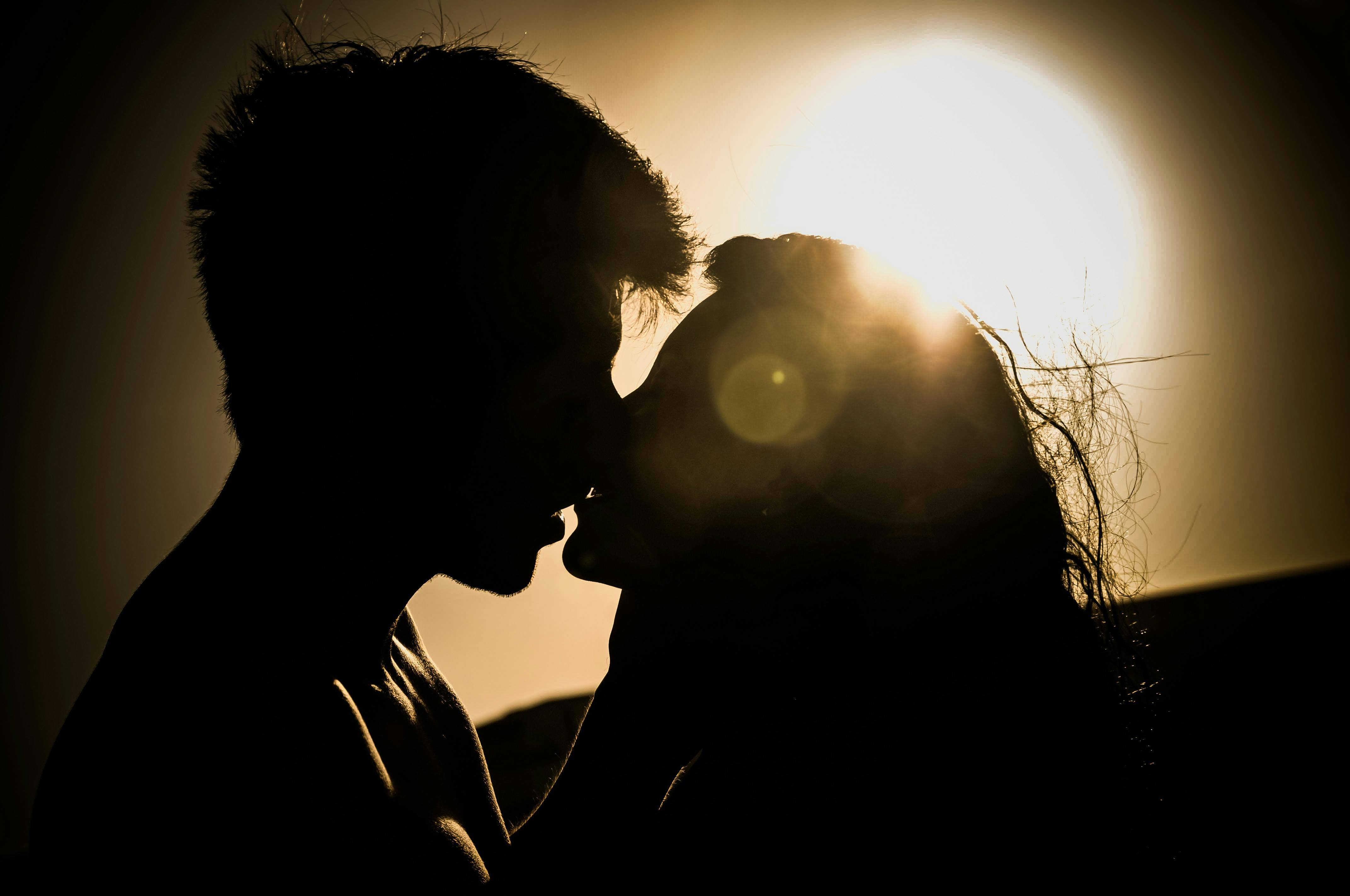 Silhouette of a couple kissing with the sun setting in the background, creating a romantic atmosphere.