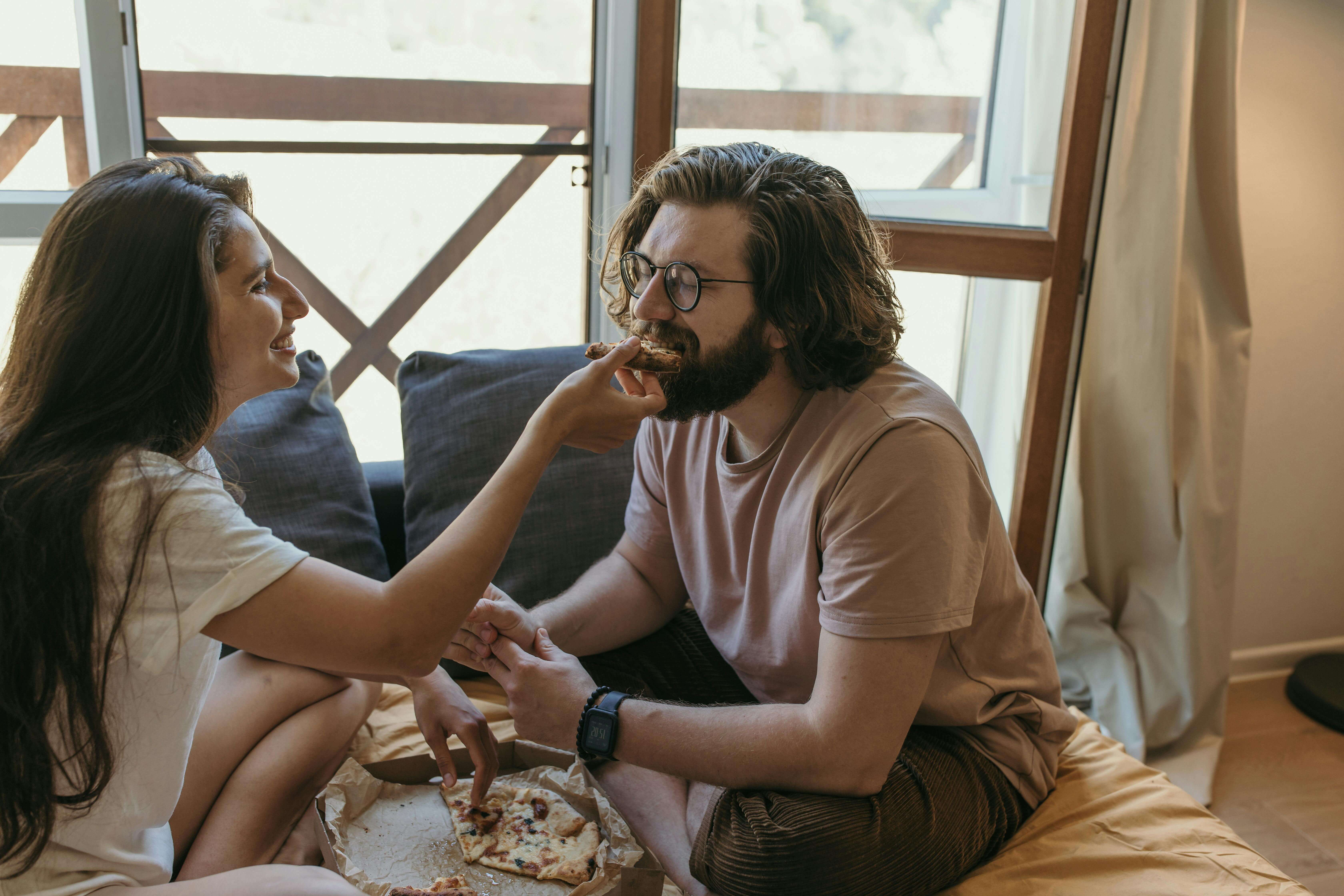 A couple shares a pizza indoors, capturing a moment of affection and togetherness.