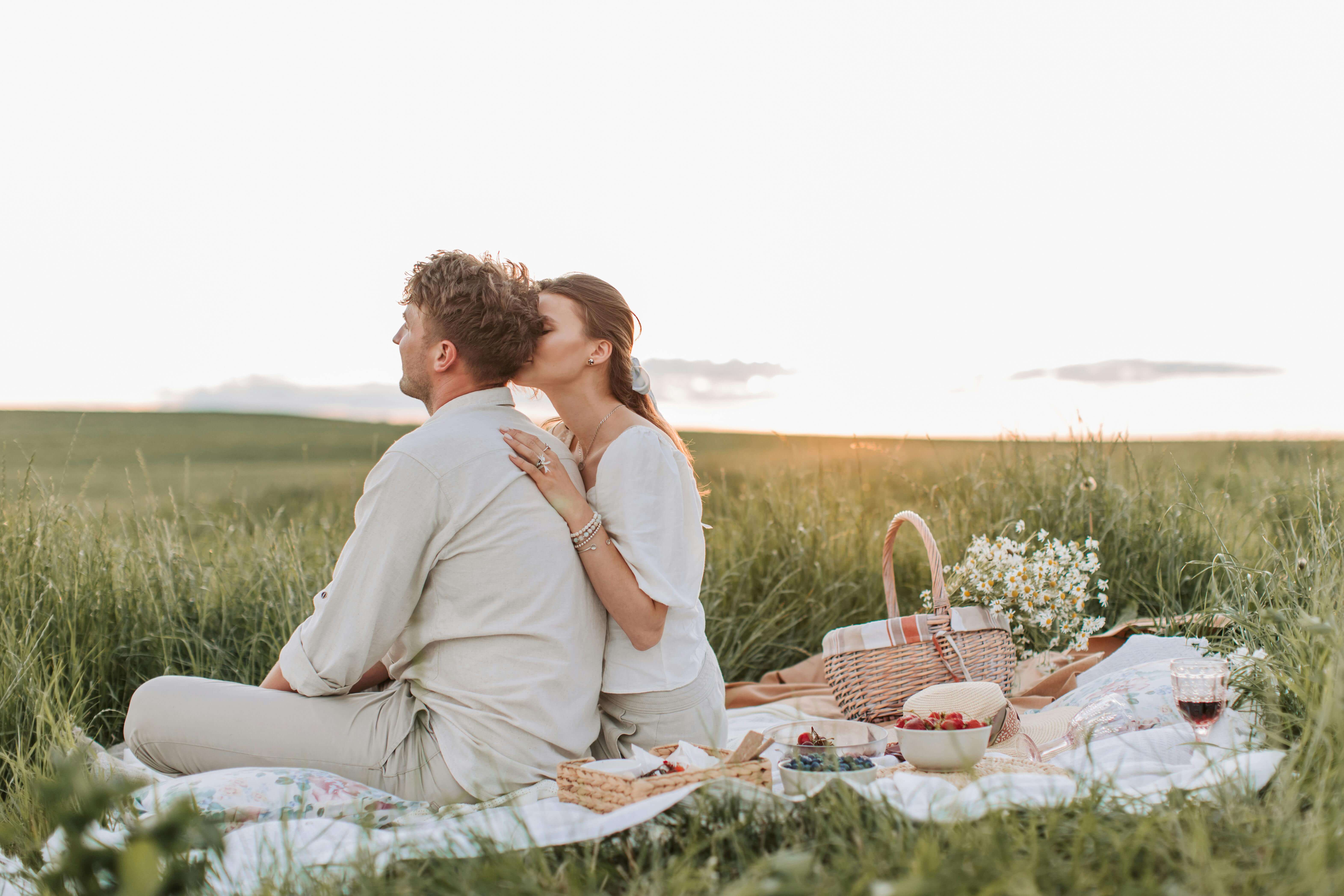 Couple enjoying a romantic picnic in a serene field at sunset, capturing love and tranquility.